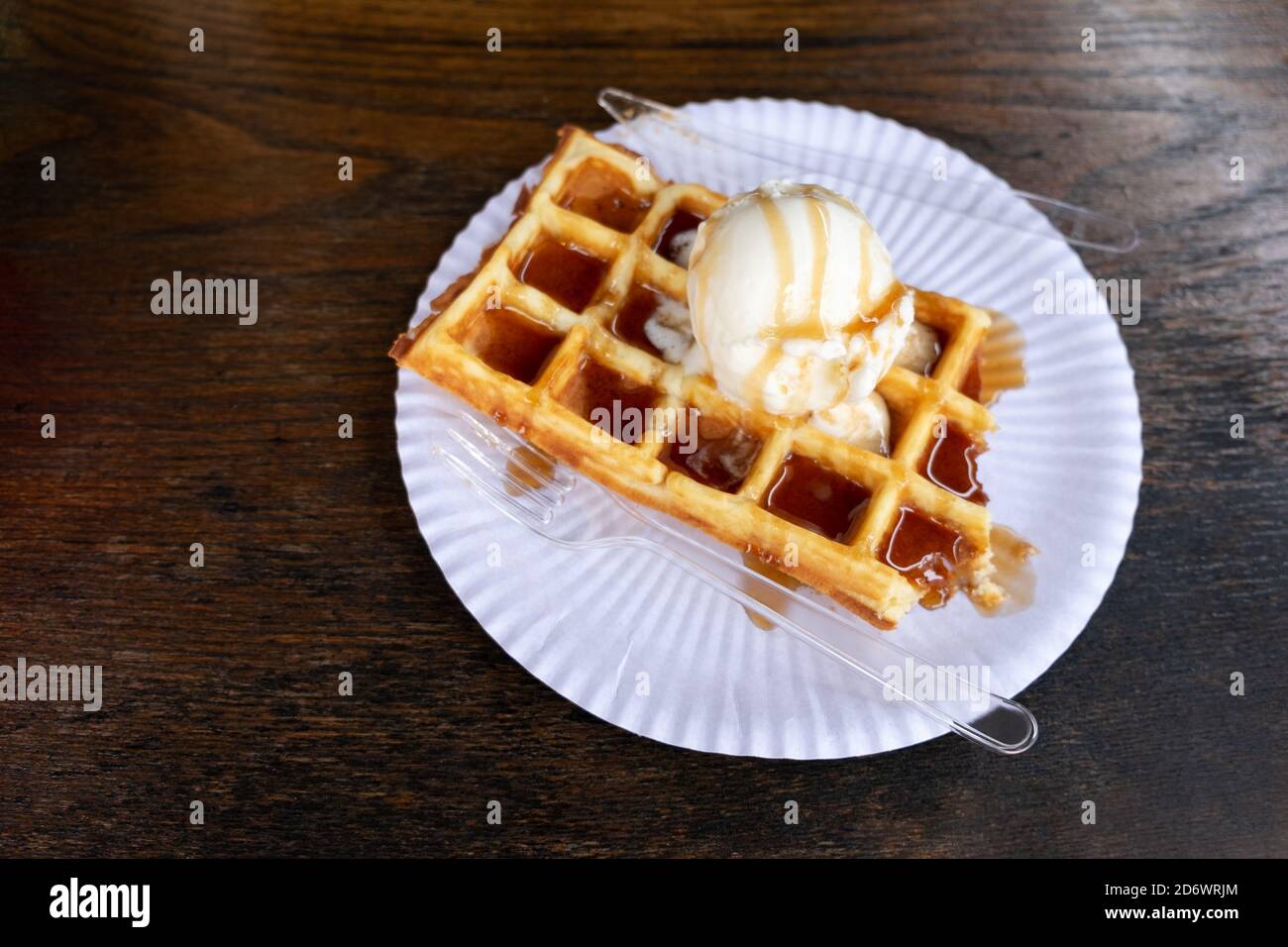 Dessert Belgian waffle with a ball of creamy ice cream poured with caramel syrup on a wooden background, in a street cafe at the Christmas market. Con Stock Photo