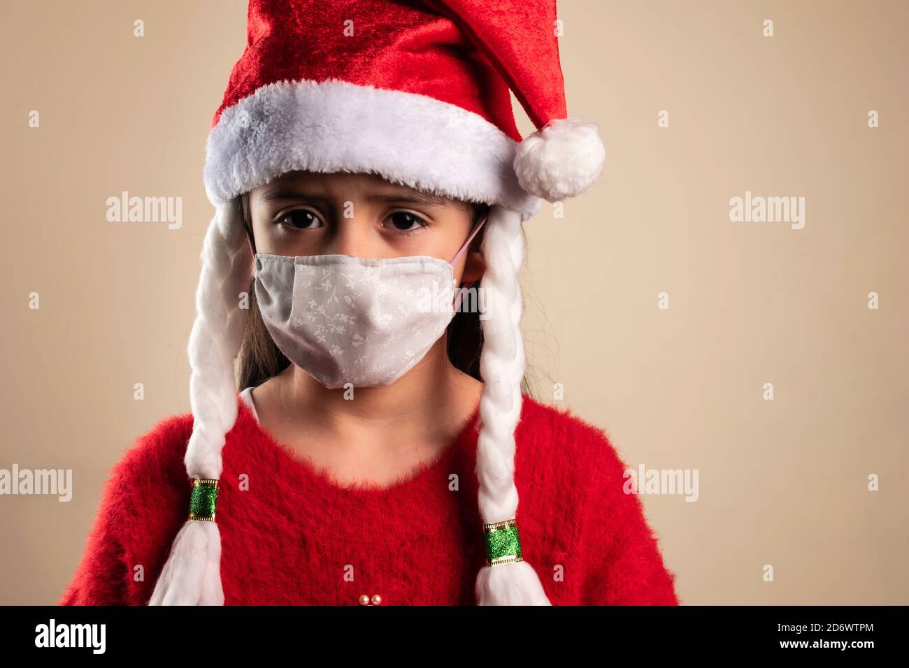 Sad girl wearing a red Santa Claus hat with braids and a face mask Stock Photo