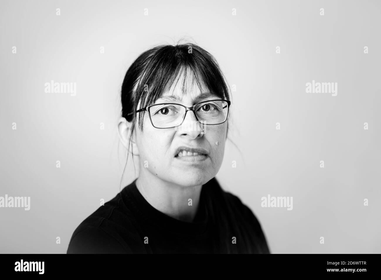 Mono, black & white, front close up of one isolated grumpy woman looking directly at camera snarling, looking fed up, disappointed. Female face snarl. Stock Photo