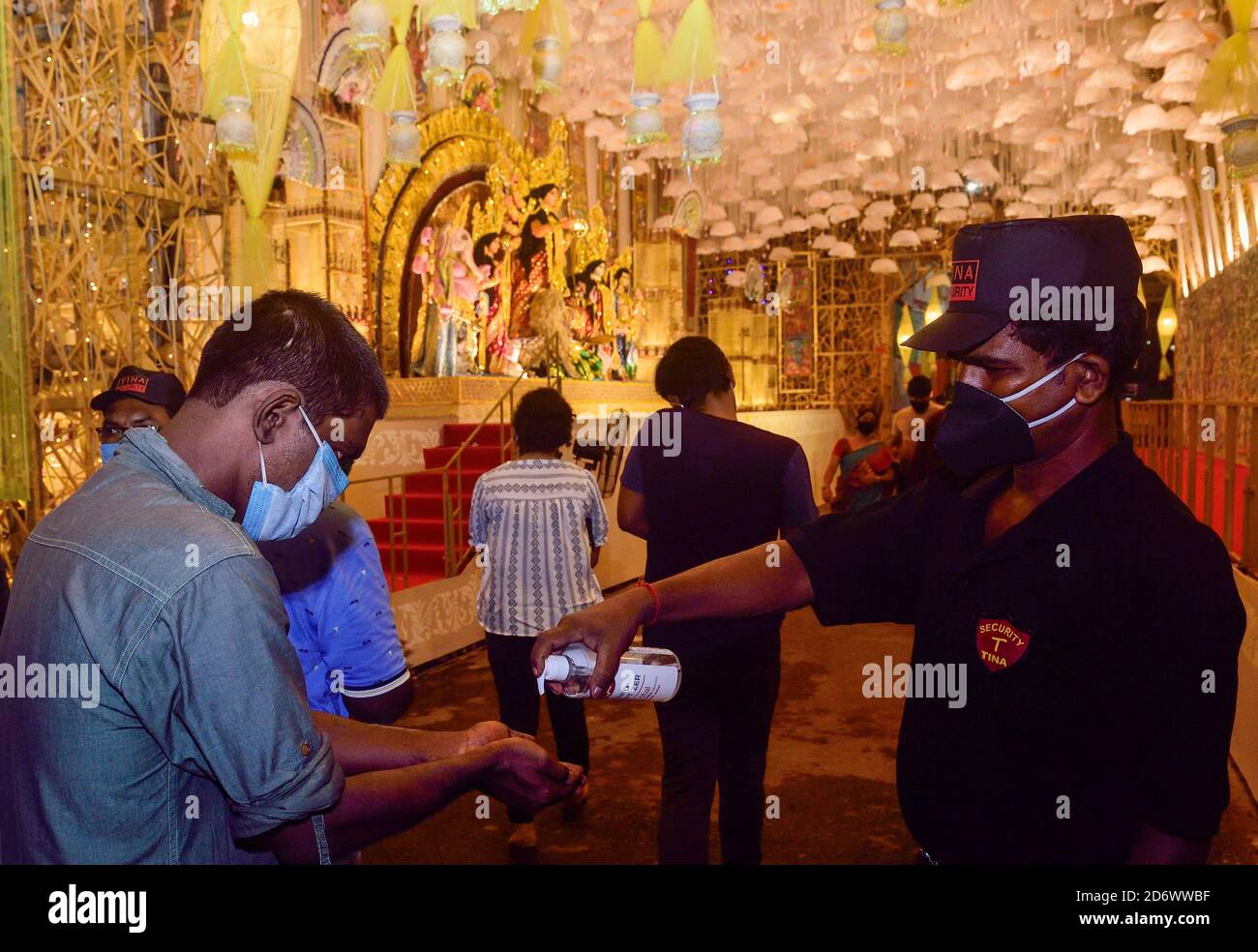 A security guard wearing a facemask sanitizes visitors hands at the entrance of Puja Pandal to stop the spread of  coronavirus. Kolkata High Court ordered this evening that all puja pandals will be considered as No entry and containment zones. Only a selective number of Puja committee members will be allowed inside however with 5-meter distance from small pandals and 10-meters from big pandal barricade to control the huge number of people. Stock Photo