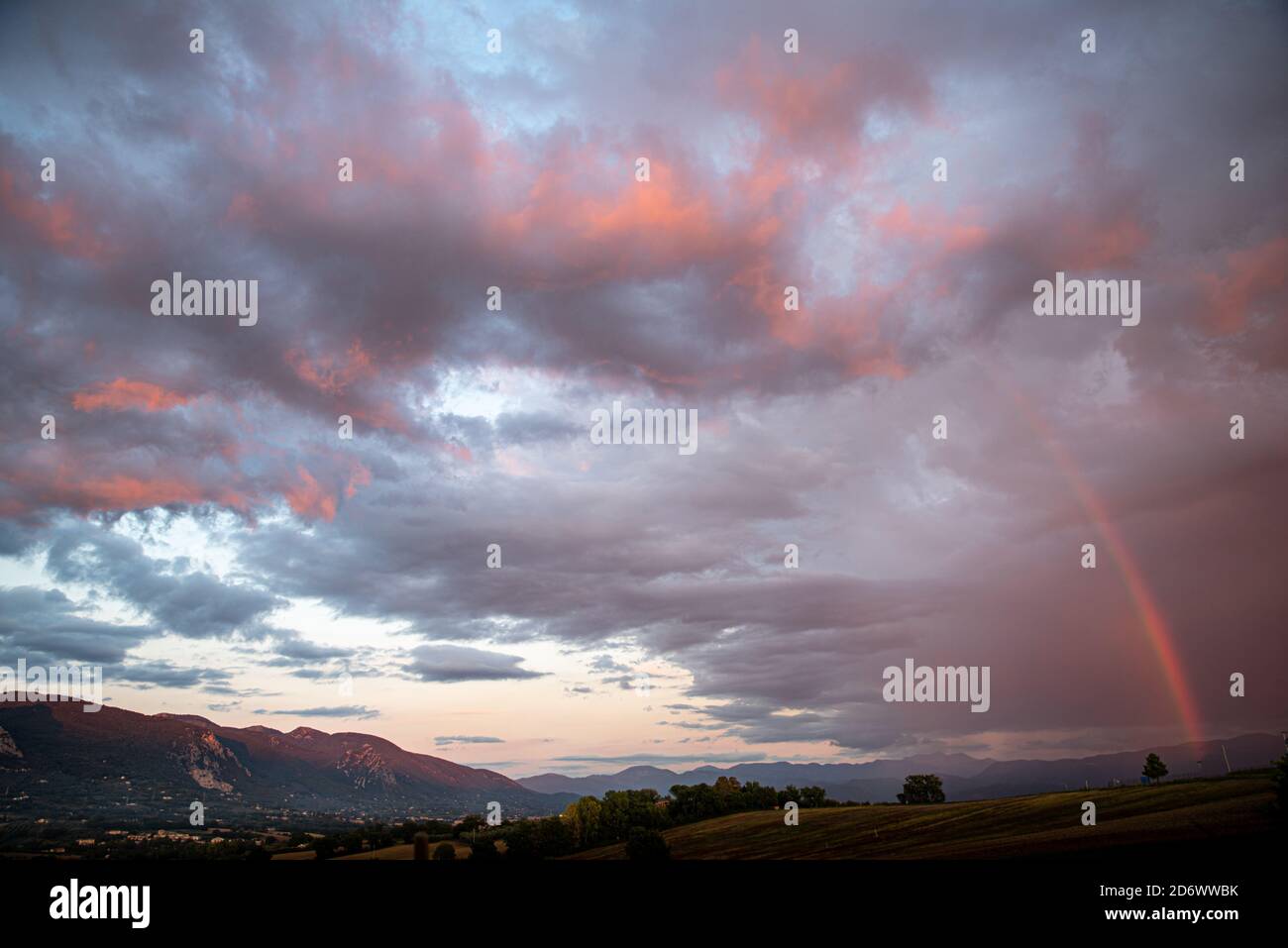 Dramatic sky panorama at sunset. Fire red clouds over the mountains and rainbow. Stock Photo