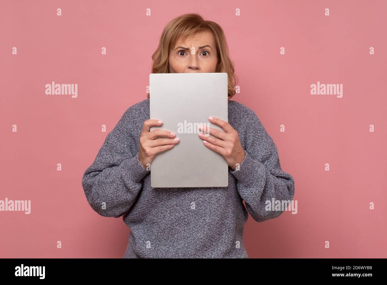 woman holding laptop being scared with a surprise face, afraid hiding her emotions Stock Photo