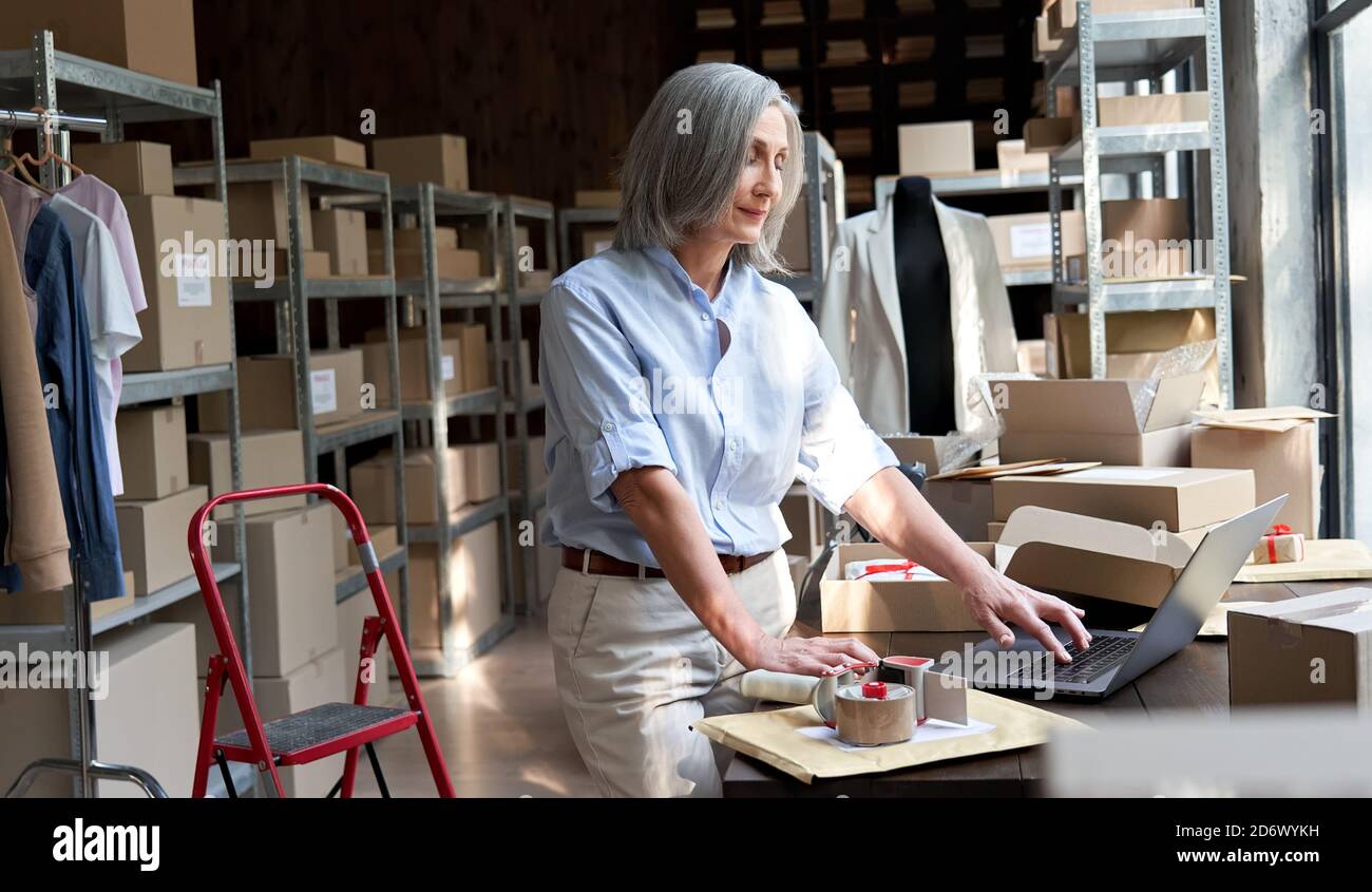 Older business woman seller using laptop checking ecommerce dropshipping orders. Stock Photo