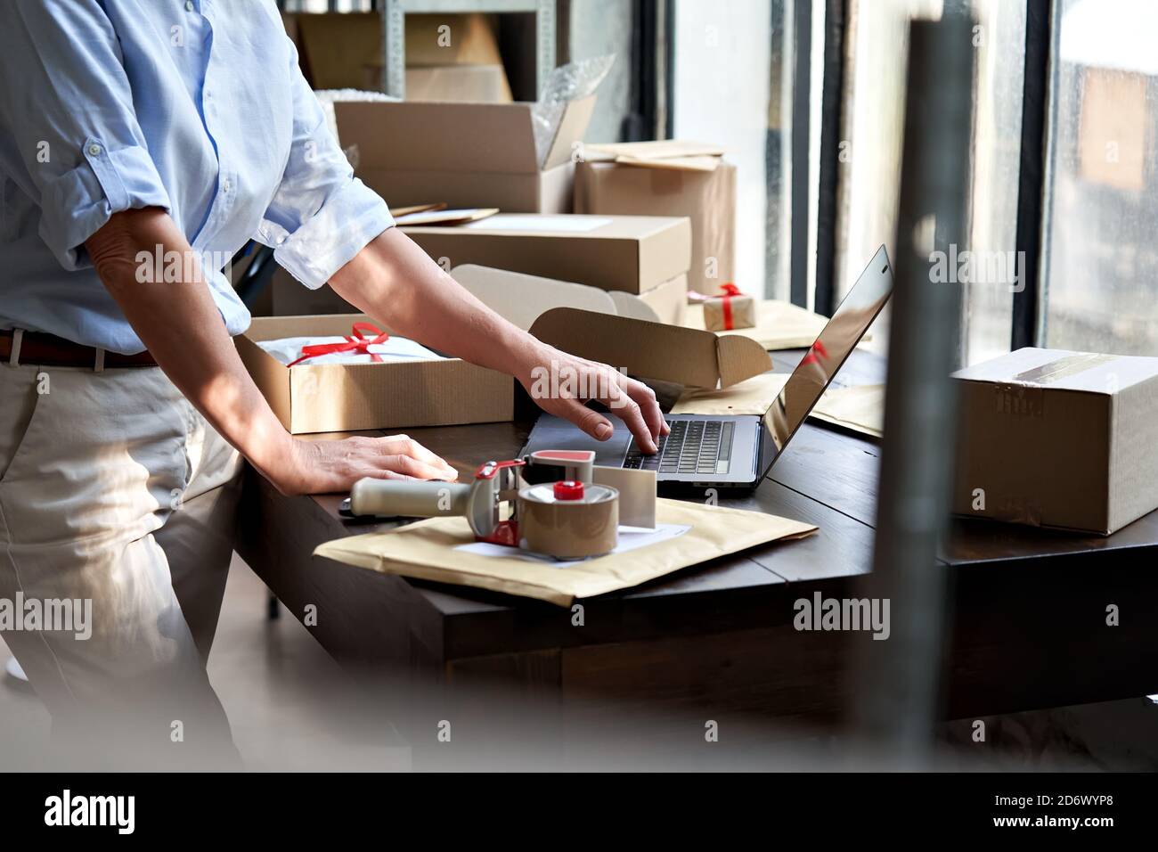 Female online business owner packing shipping ecommerce parcel using laptop. Stock Photo
