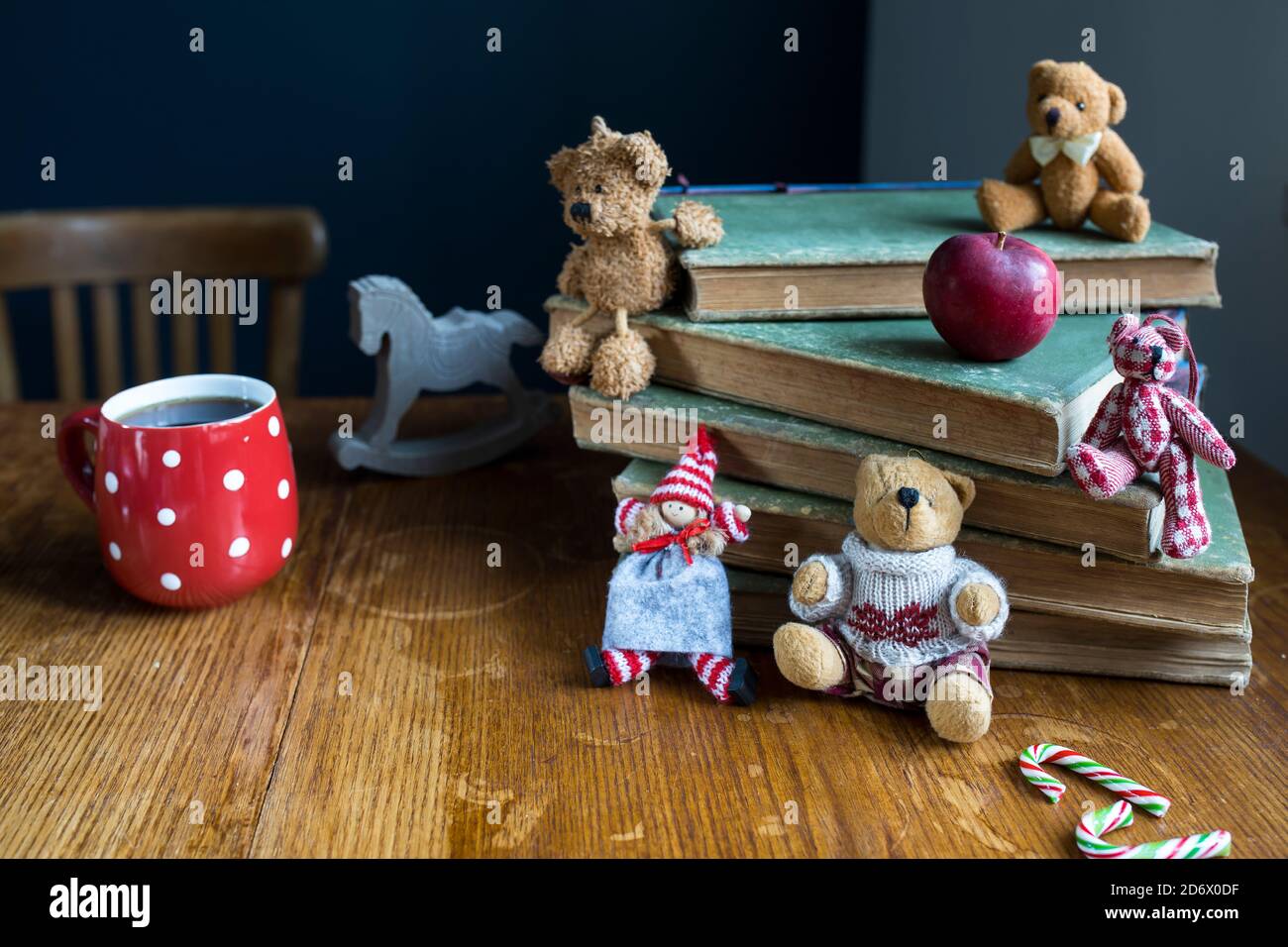 A Christmas doll and bears sit on a stack of old books. Copy space. Selective focus. Red cup with white polka dots with tea. Stock Photo