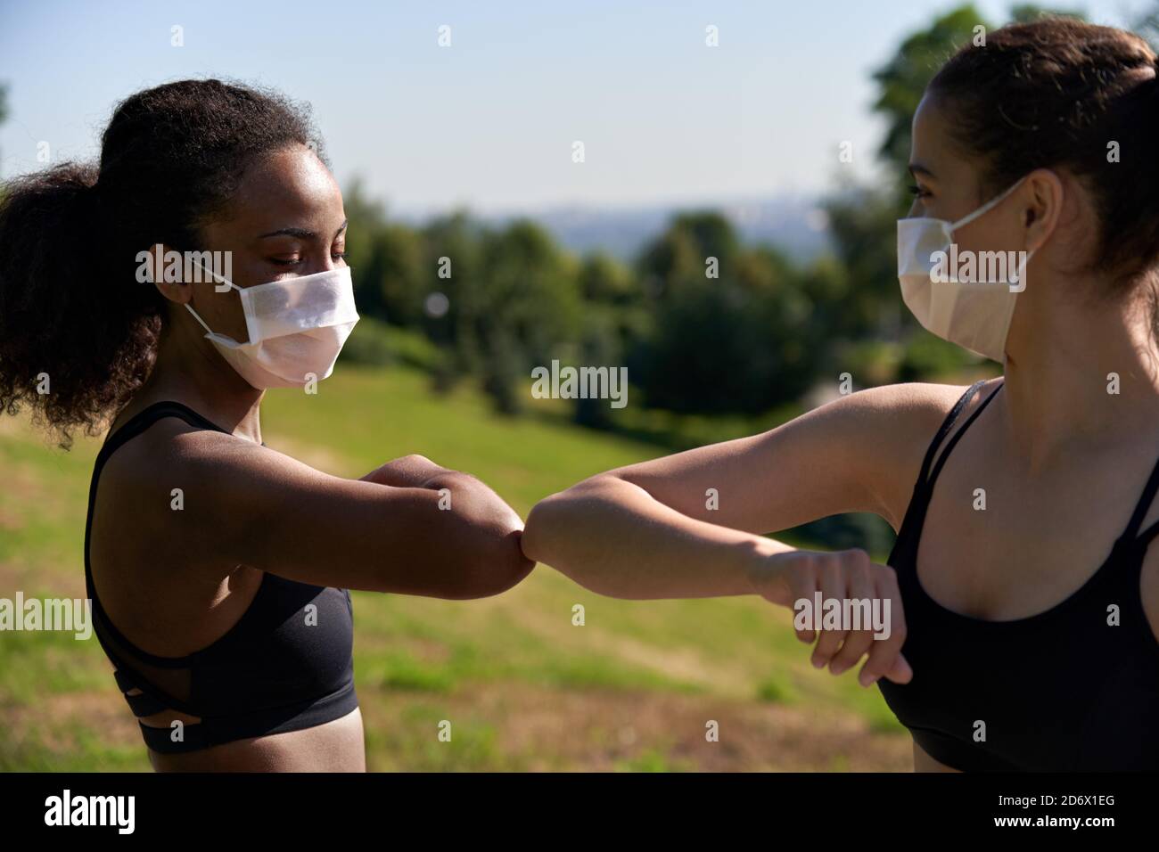 African and indian fit sporty ladies friends wear face masks give elbow bump. Stock Photo