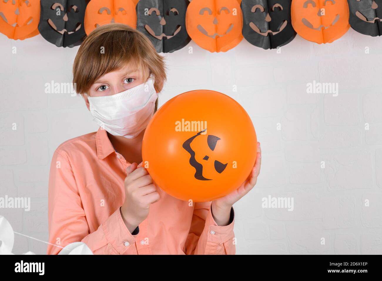 A blond boy in protective medical mask looking at orange balloon, Happy Halloween on quarantine coronavirus pandemic Stock Photo