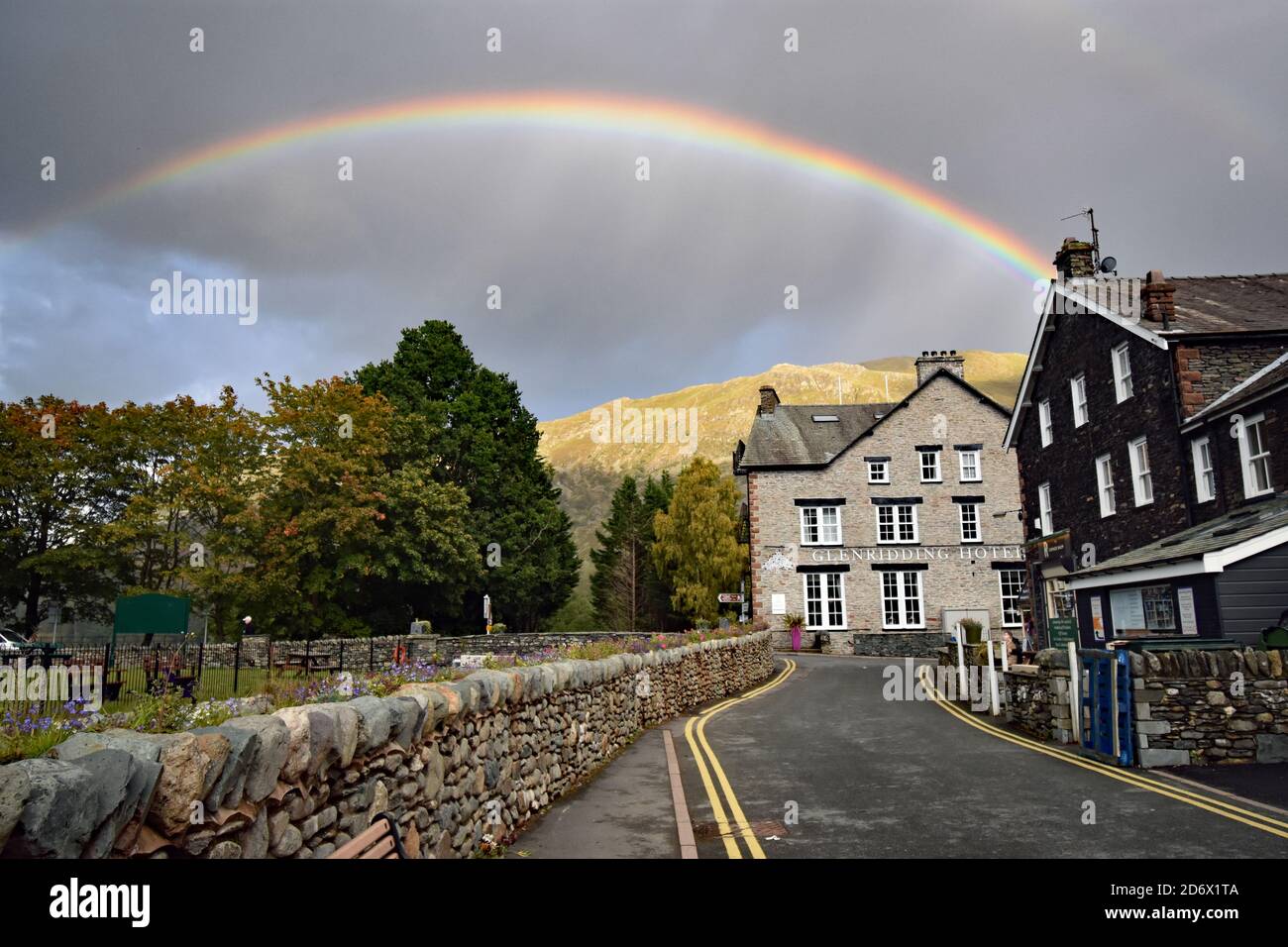A rainbow above the Glenridding Hotel on the edge of Ullswater in the Lake District National Park.  A stone wall lines the road leading to the hotel. Stock Photo