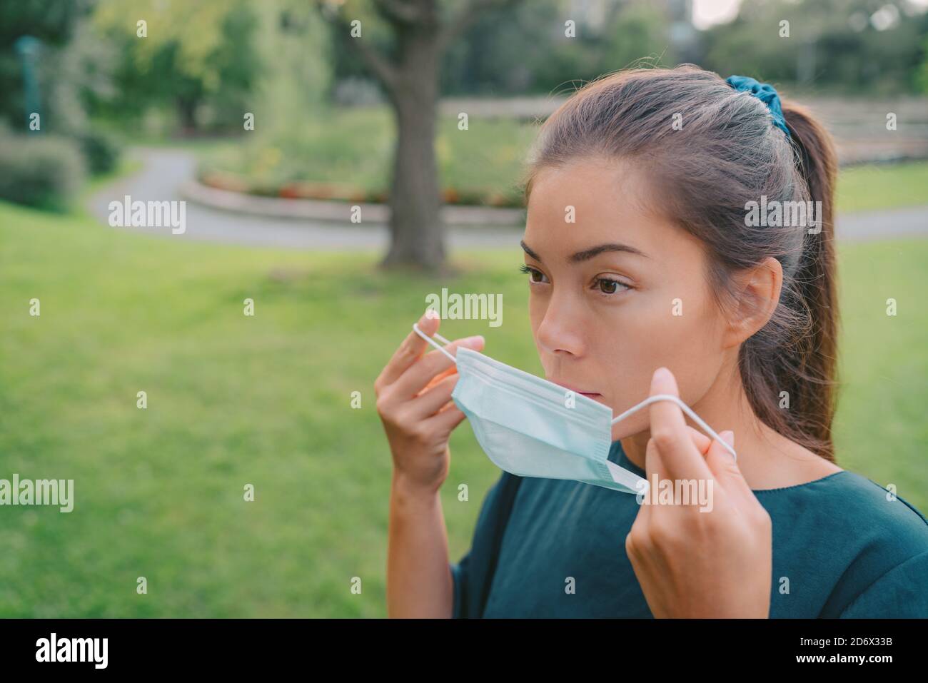 Woman putting on a surgical face mask for coronavirus prevention. Serious Asian girl using medical grade covering Stock Photo
