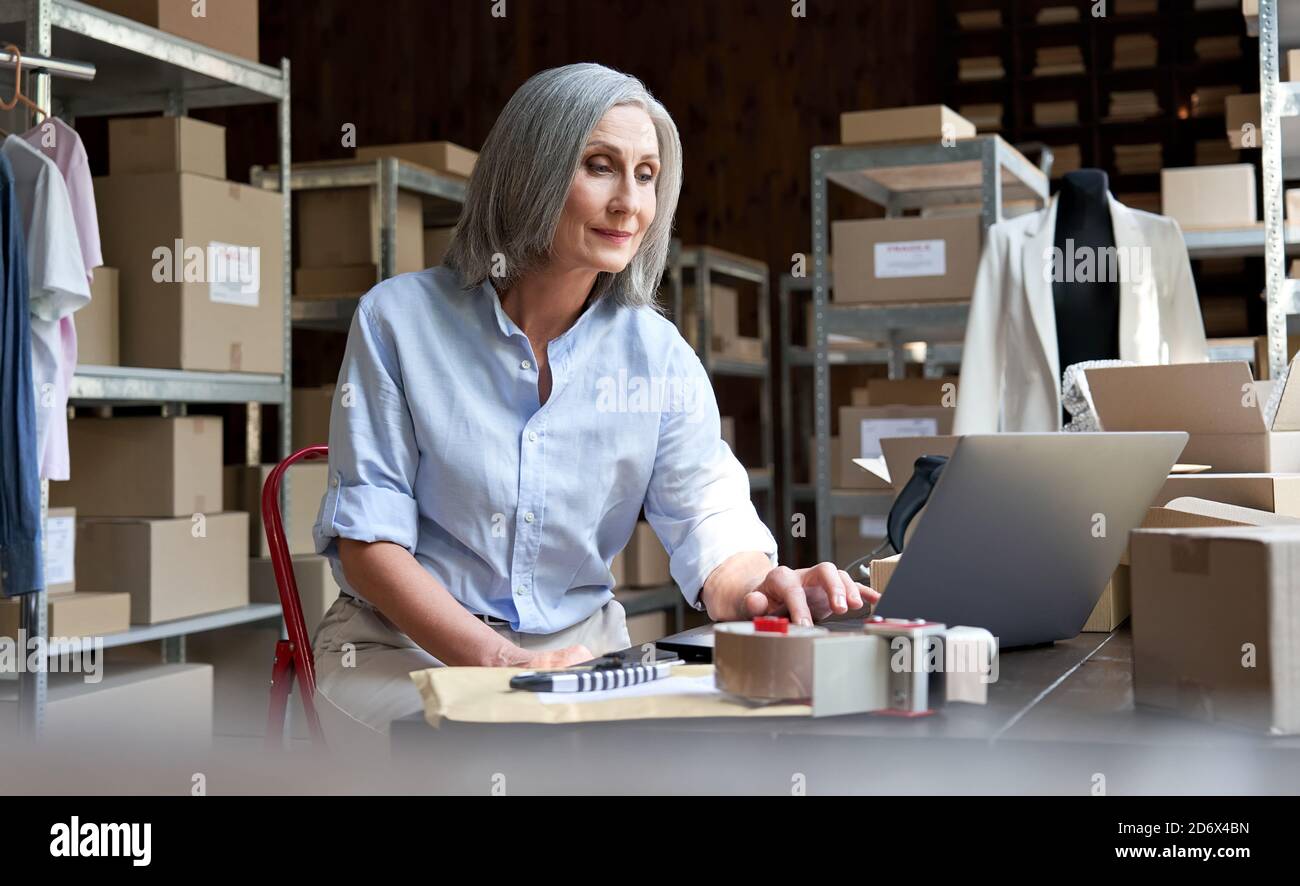 Mature female seller using computer checking ecommerce clothing orders. Stock Photo