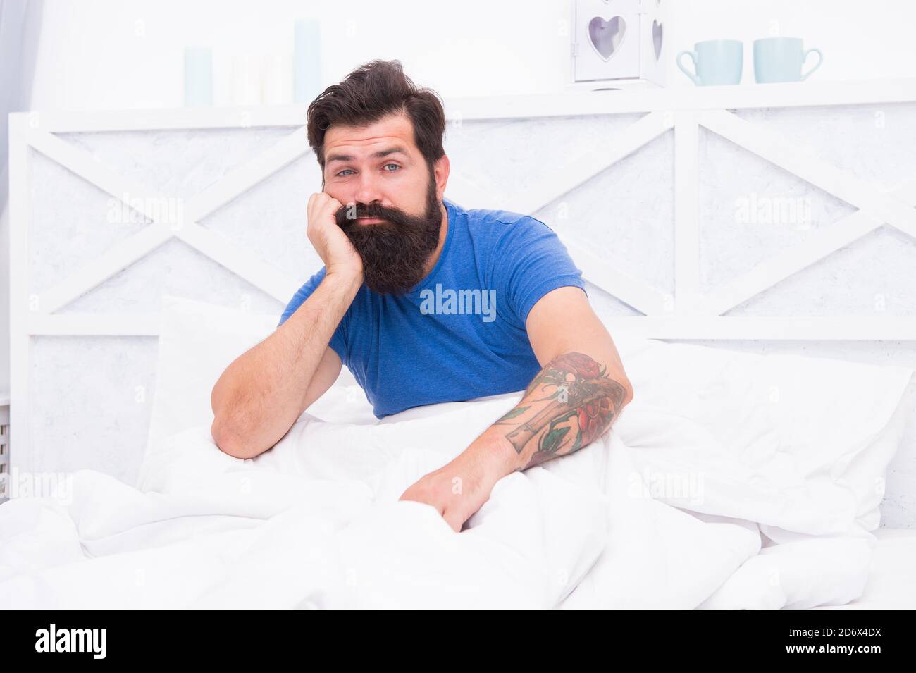 unshaven caucasian man woke up alone in bed with white linen at home, bedtime. Stock Photo