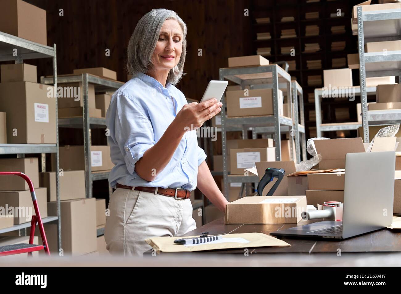 Female small business owner using mobile app on smartphone checking parcel box. Stock Photo