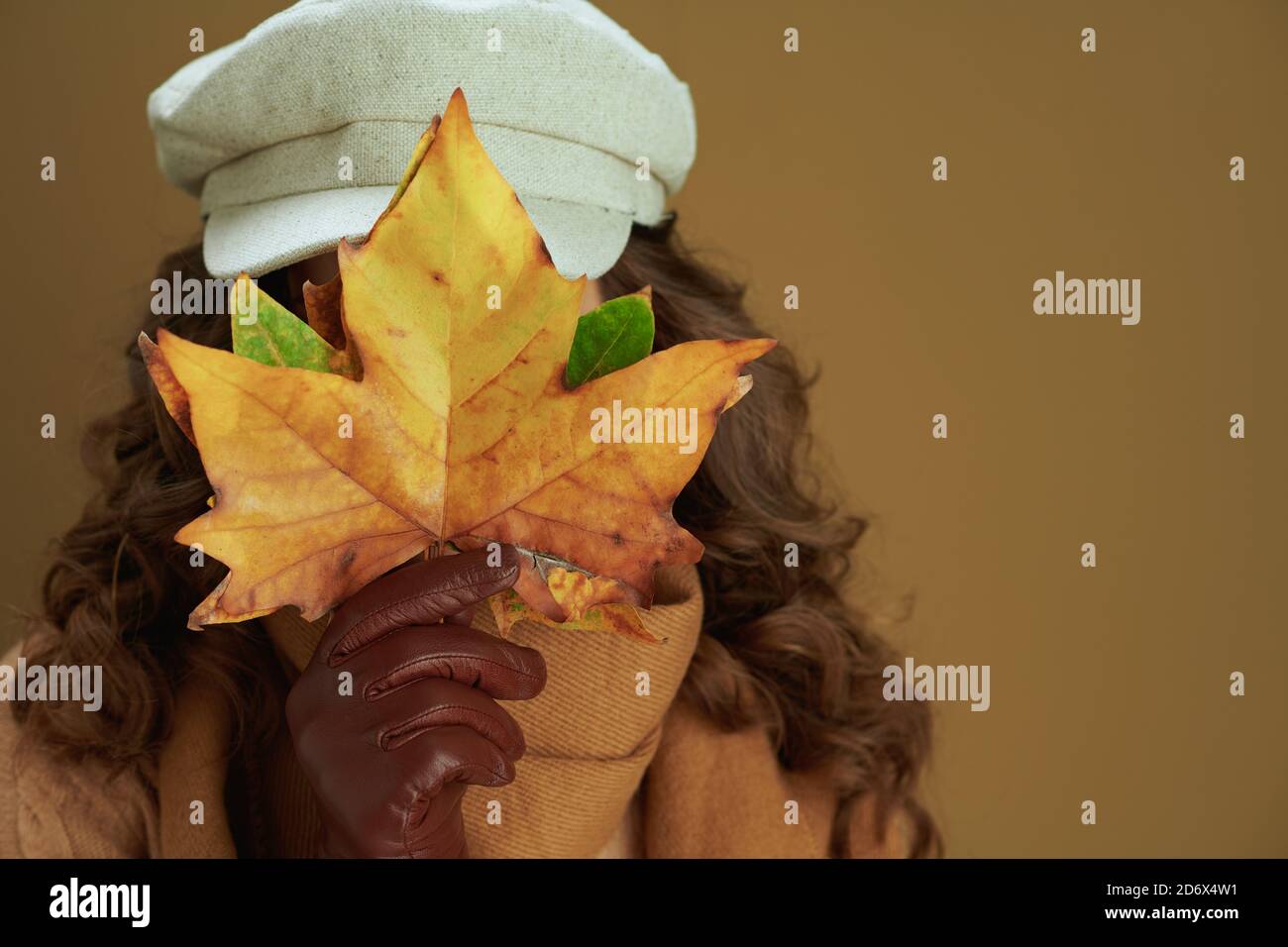 Hello september. 40 years old woman in scarf with leather gloves and yellow autumn maple leaves isolated on beige background. Stock Photo