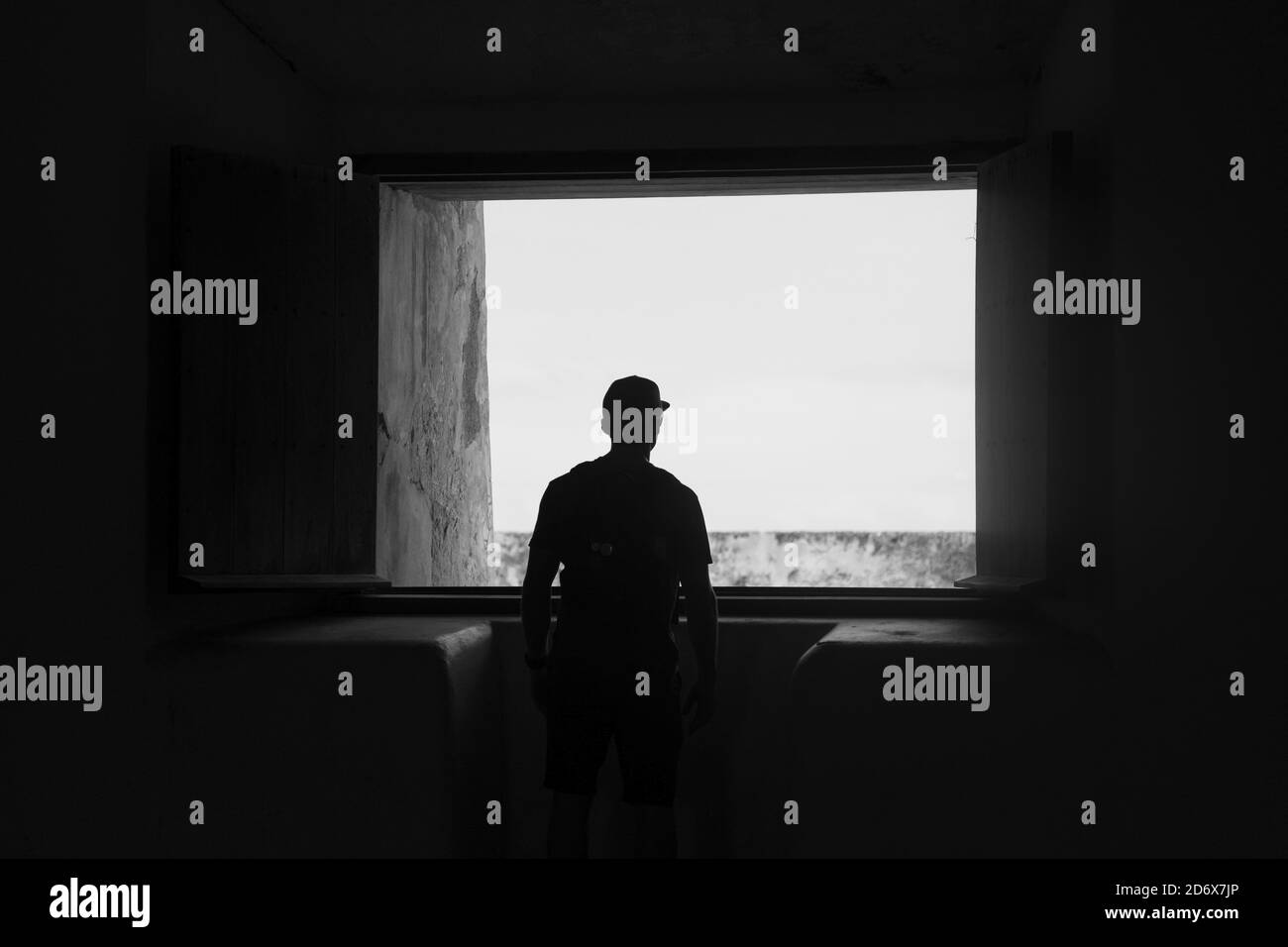 Grayscale shot of a silhouetted person looking out of the window Stock Photo