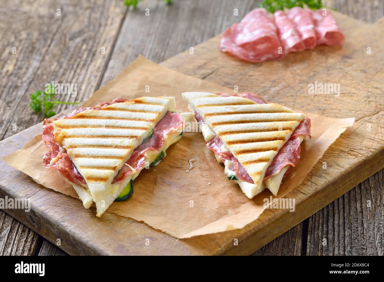 Pressed and toasted double panini with Italian salami and cheese served on sandwich paper on a wooden table Stock Photo