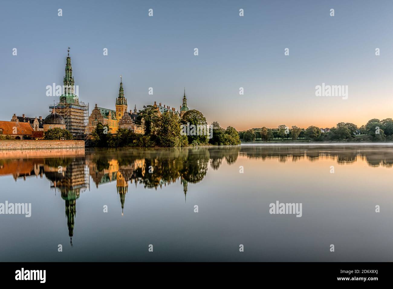 the mirror-shiny lake of Frederiksborg with reflections of the enlightened castle at sunrise, Hillerod, Denmark, October 17, 2020 Stock Photo