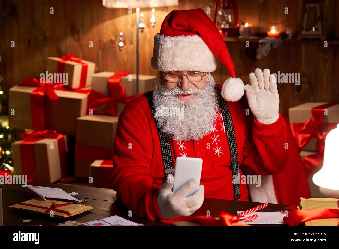 Santa Claus video calling holding smartphone sitting at home table. Stock Photo