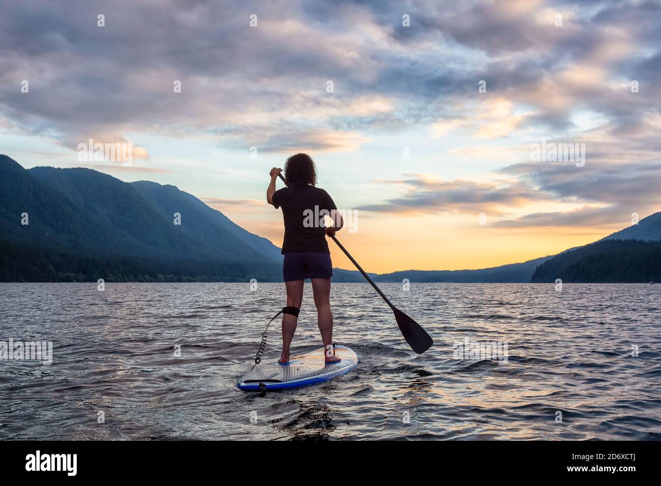 Woman Paddleboarding on Scenic Lake at Sunset Stock Photo