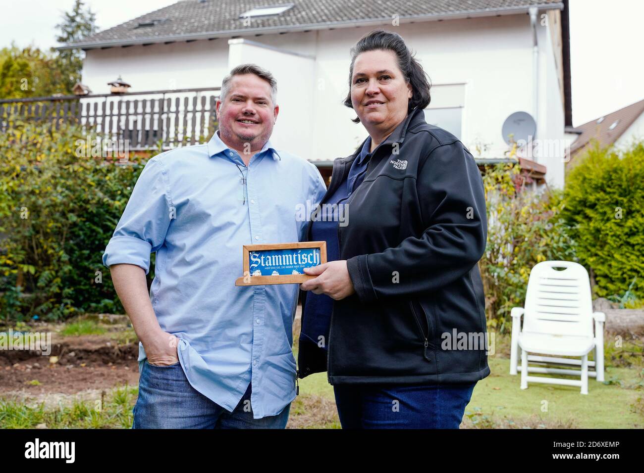 Ramstein Miesenbach, Germany. 14th Oct, 2020. Will and Bianka Pfannenstiel are standing in the garden in front of their house and hold a sign in their hands that says 'Stammtisch'. (to dpa 'Between Trump and drones: In Ramstein the election fever is slowly rising') Credit: Uwe Anspach/dpa/Alamy Live News Stock Photo