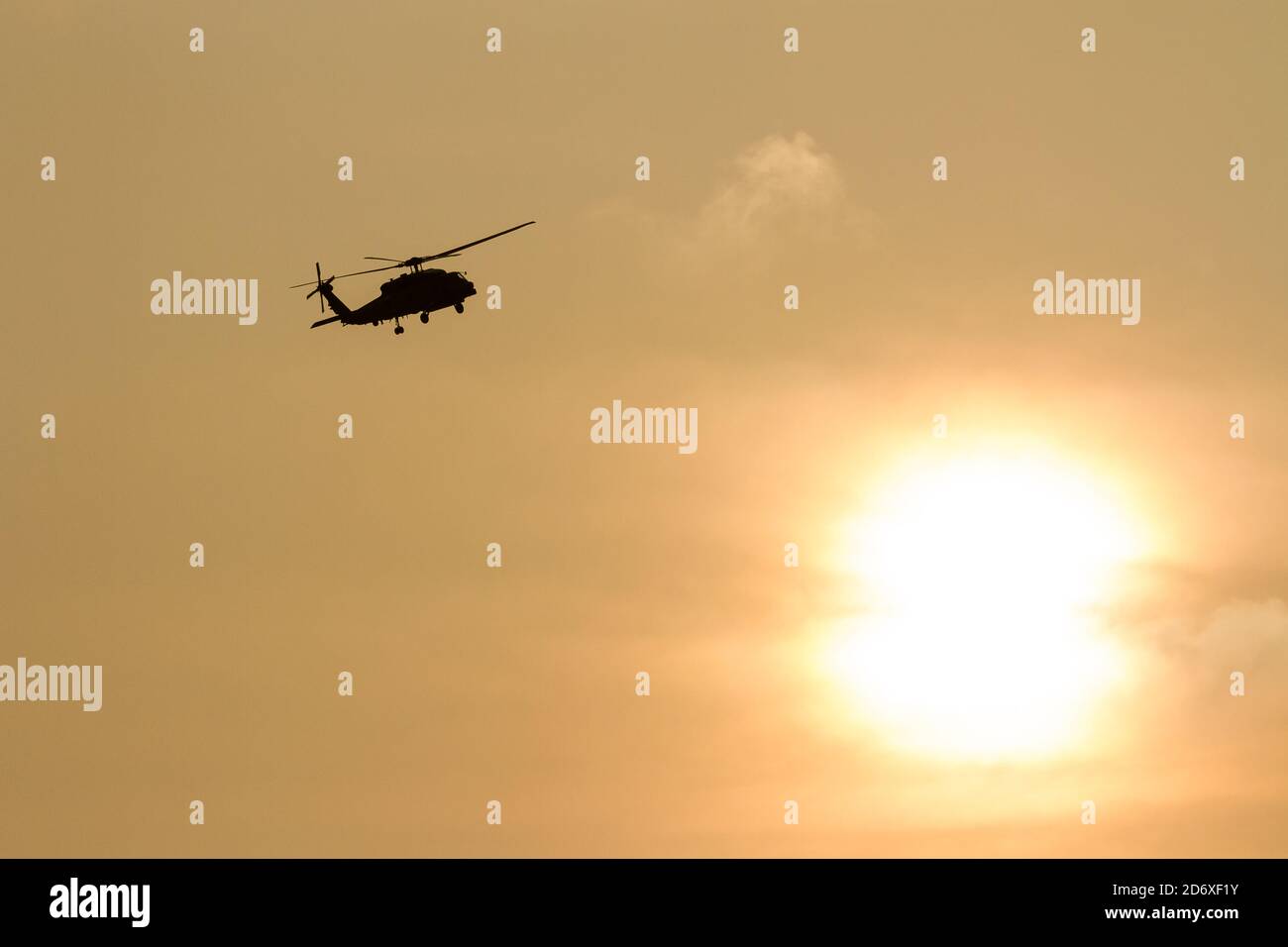 A silhouetted Sikorsky SH-60 Seahawk helicopter, of Carrier Air Wing Five, flying in front a cloudy sunset, Kanagawa, Japan. Stock Photo