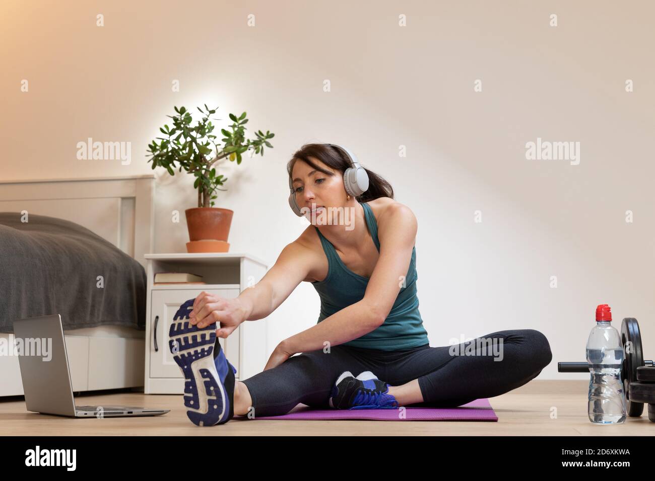 Beautiful women doing fitness at home near bed and watching online tutorials on laptop in natural light. Sport and recreation concept. Stock Photo