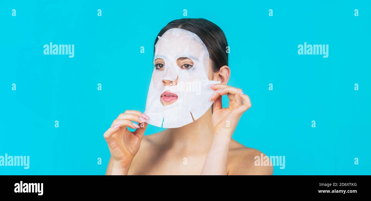 Moisturizing mask. Anti aging procedure. Woman applying sheet mask on her face, on blue background. Beautiful woman with mask Stock Photo