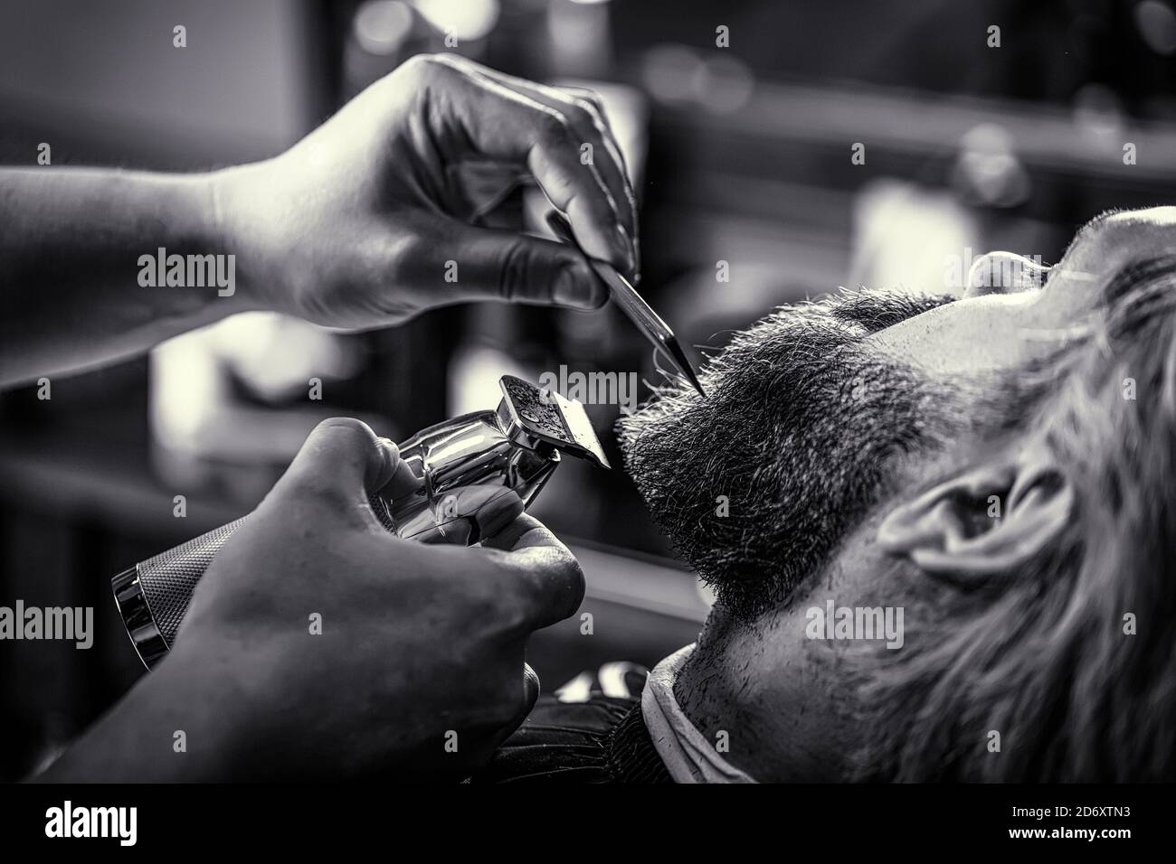 Barber works with a beard clipper. Hipster client getting haircut