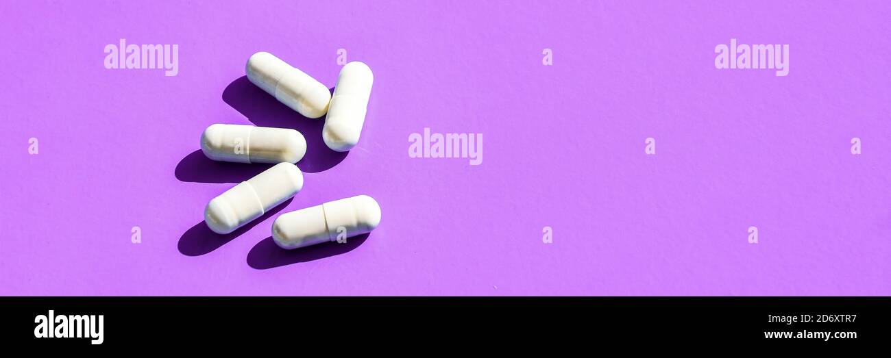 White capsule pills on purple background with hard light and shadows