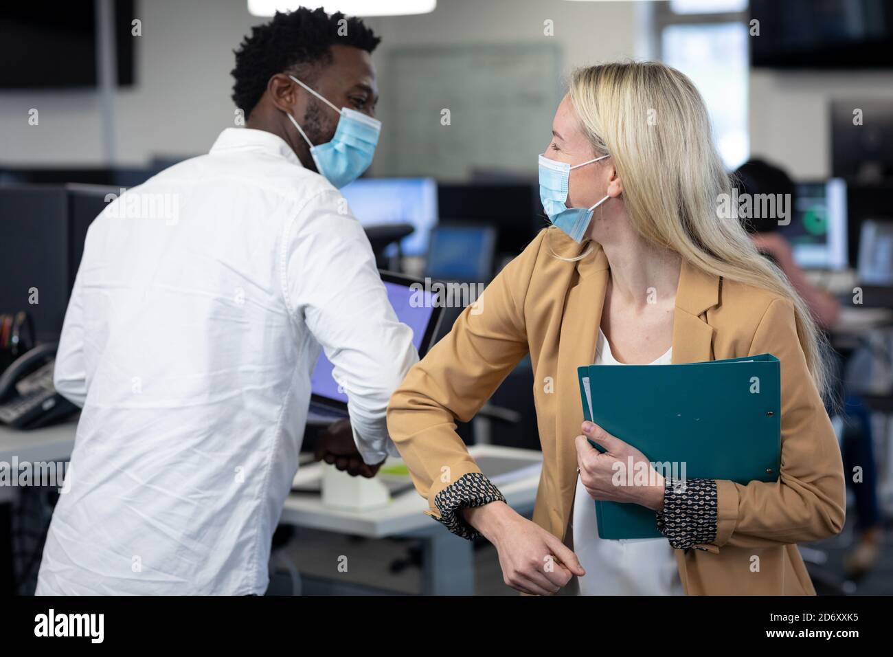 Businessman and businesswoman wearing face masks greeting each other by touch elbows at office Stock Photo