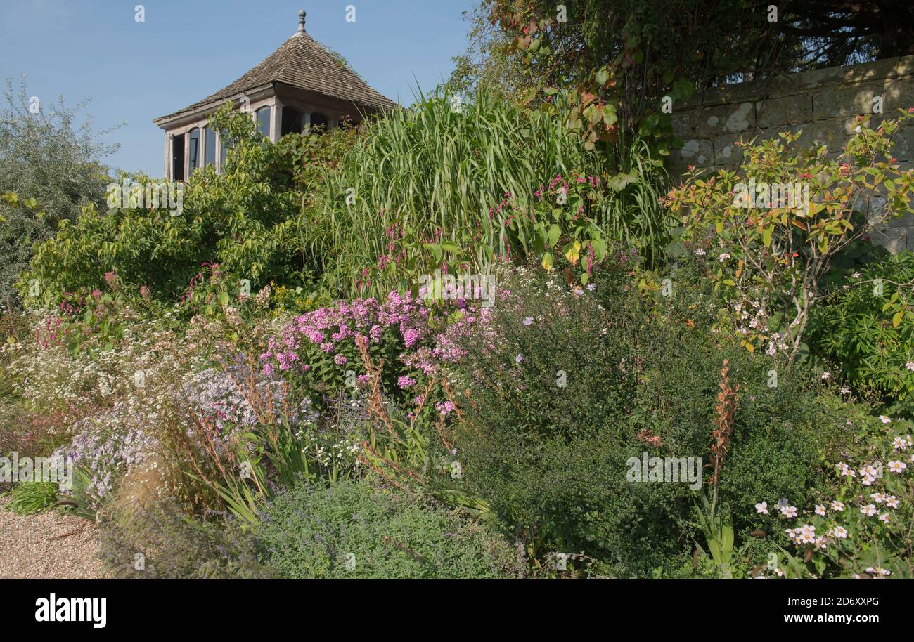 Late Summer Herbaceous Border with Pink Phlox and Ornamental Grasses with a Garden House in the Background in a Country Cottage Garden in West Sussex Stock Photo