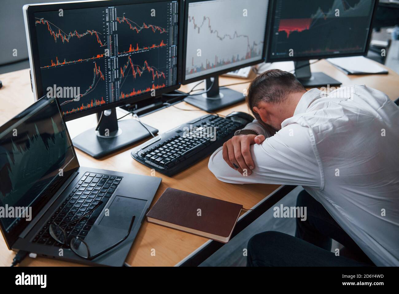 Tired businessman sleeping on the workplace by leaning on the table with  multiple screens on it. Stock information on displays Stock Photo - Alamy