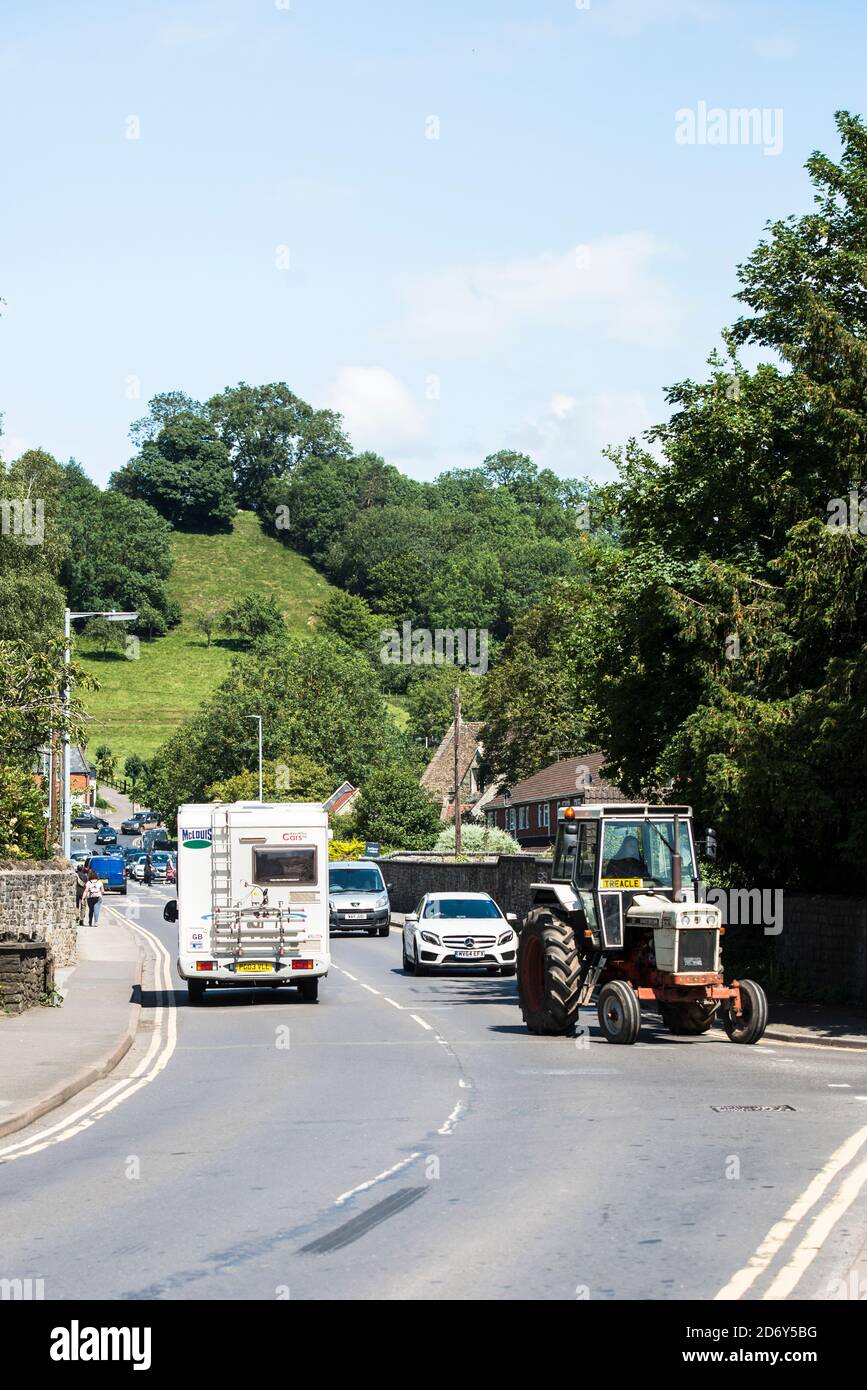 Glastonbury city center traffic on the A361 slowed by a large turning tractor. Young female drive. David Brown 1212 tractor. Stock Photo