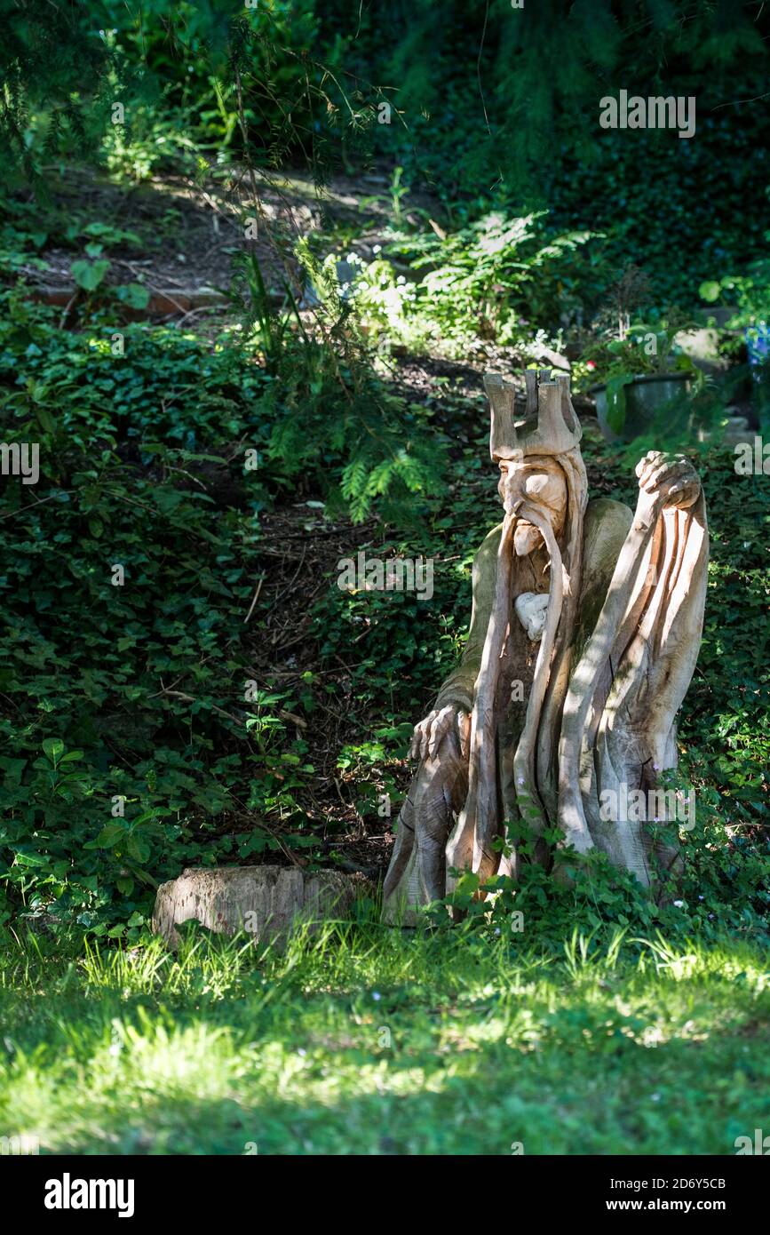 Garden Wizard carving with green wood background and beautiful filtered sunlight illuminating the statue. Garden art in a sylvan setting, Glastonbury. Stock Photo