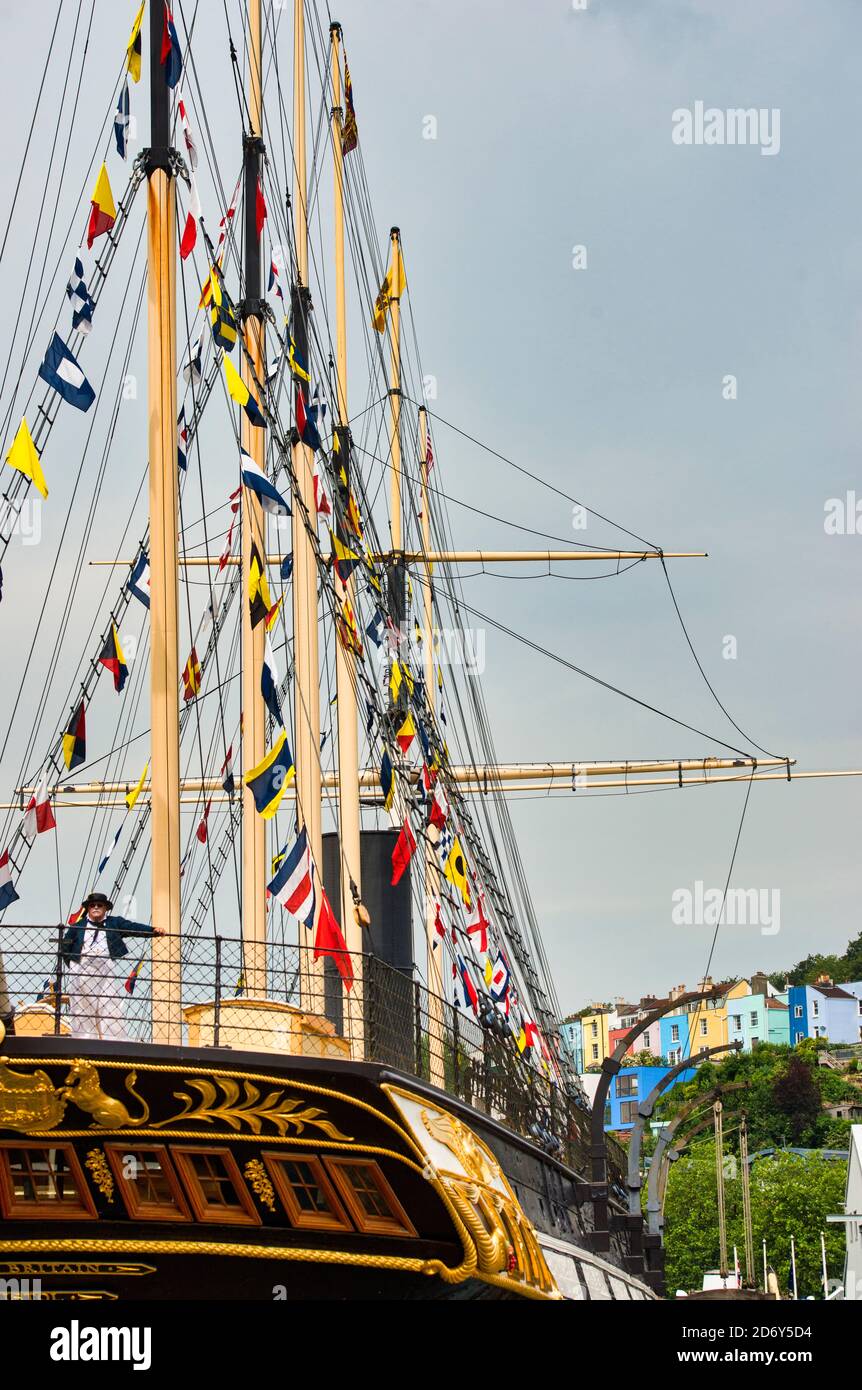 SS Great Britain stern view. Actor in dress uniform leaning on railing. Signal flags, dress ship rigging. Bristol Dockyard. GB. Colorful buildings. Stock Photo