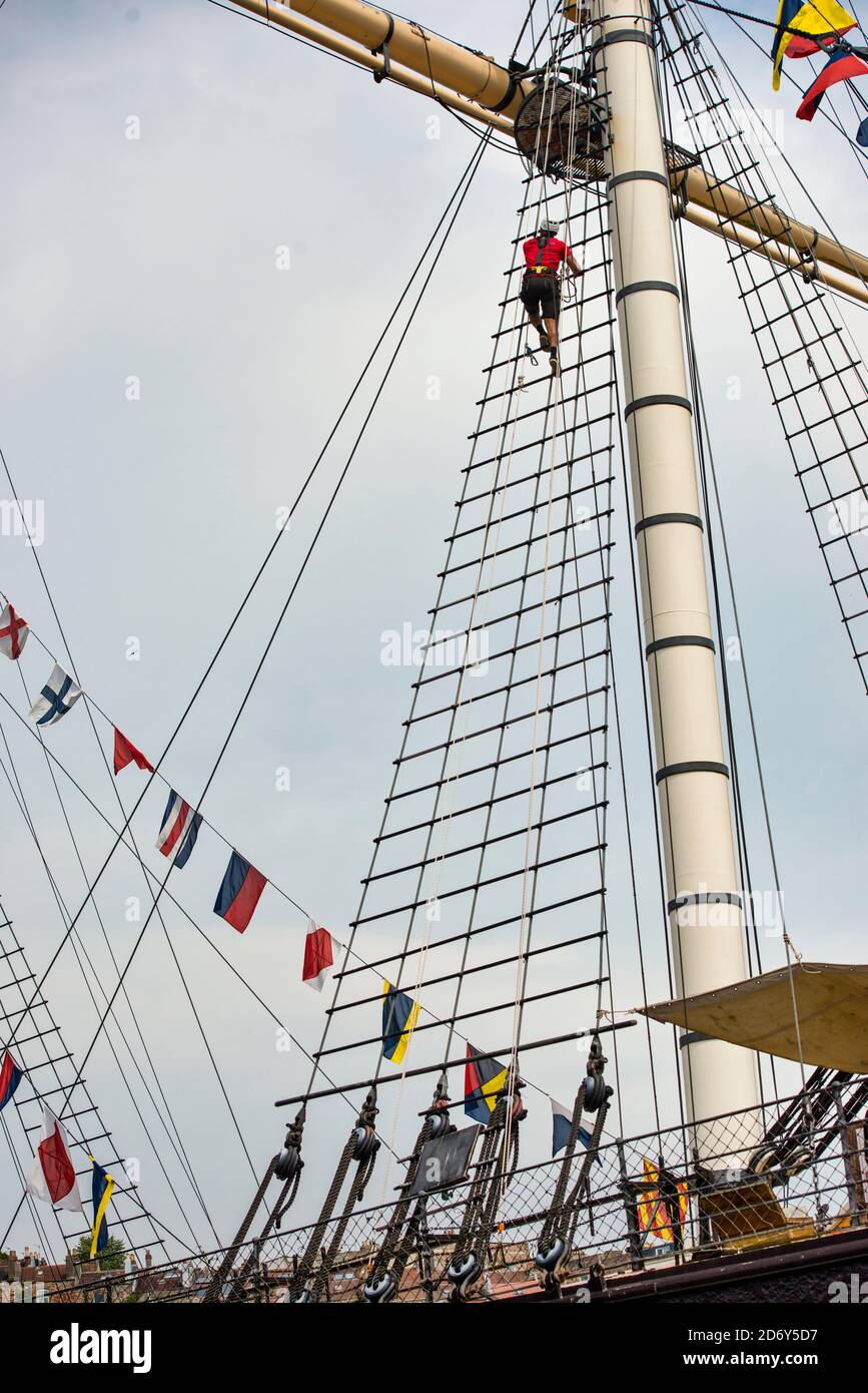 Go Aloft! SS Great Britain tourist attraction. A man is almost to the top viewing platform, climbing rigging on the mainmast on a sunny blue sky day. Stock Photo