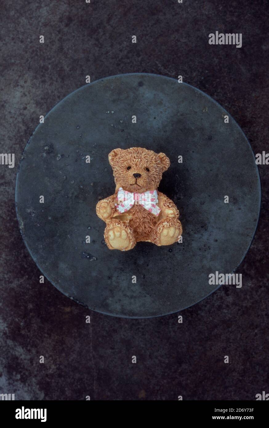 Fine detailed resin model of brown teddy bear wearing spotted pink and white bow tie lying on tarnished metal Stock Photo