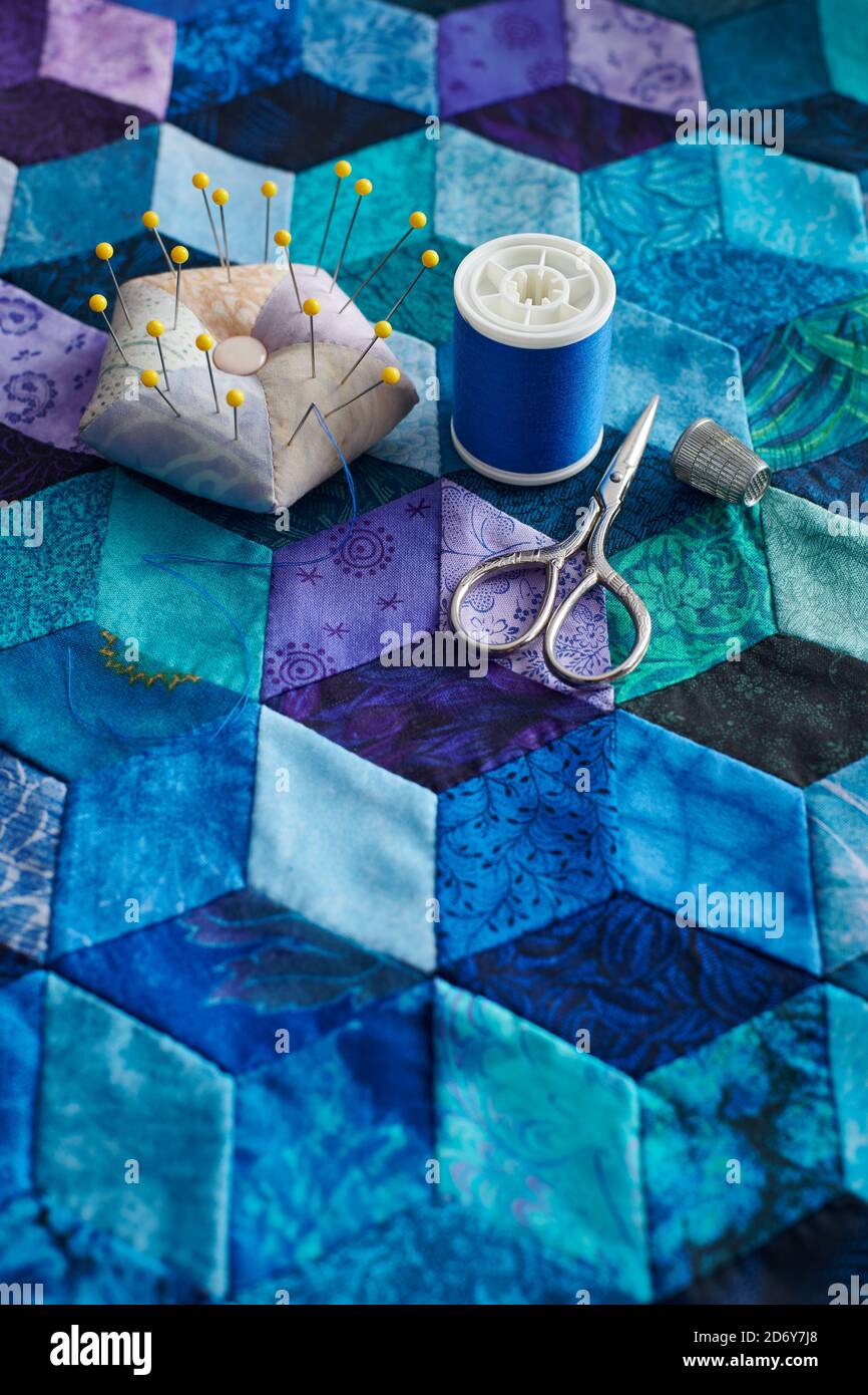 Pincushion, spool of thread, scissors and thimble on the tumbling blocks quilt background Stock Photo
