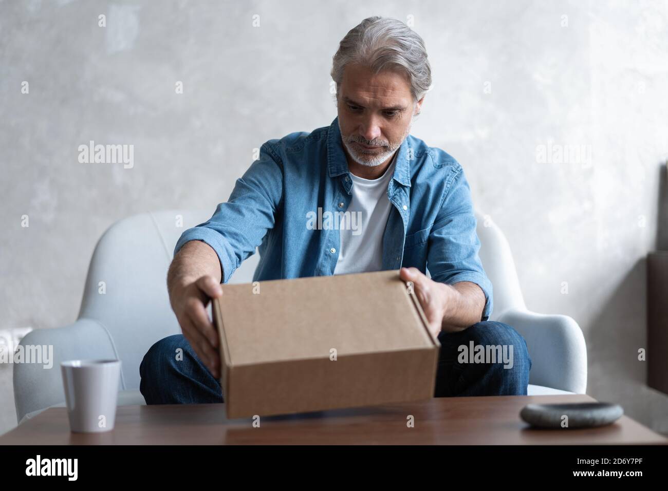 Smiling man consumer open cardboard box get postal parcel, male customer receive carton package sit on sofa at home Stock Photo