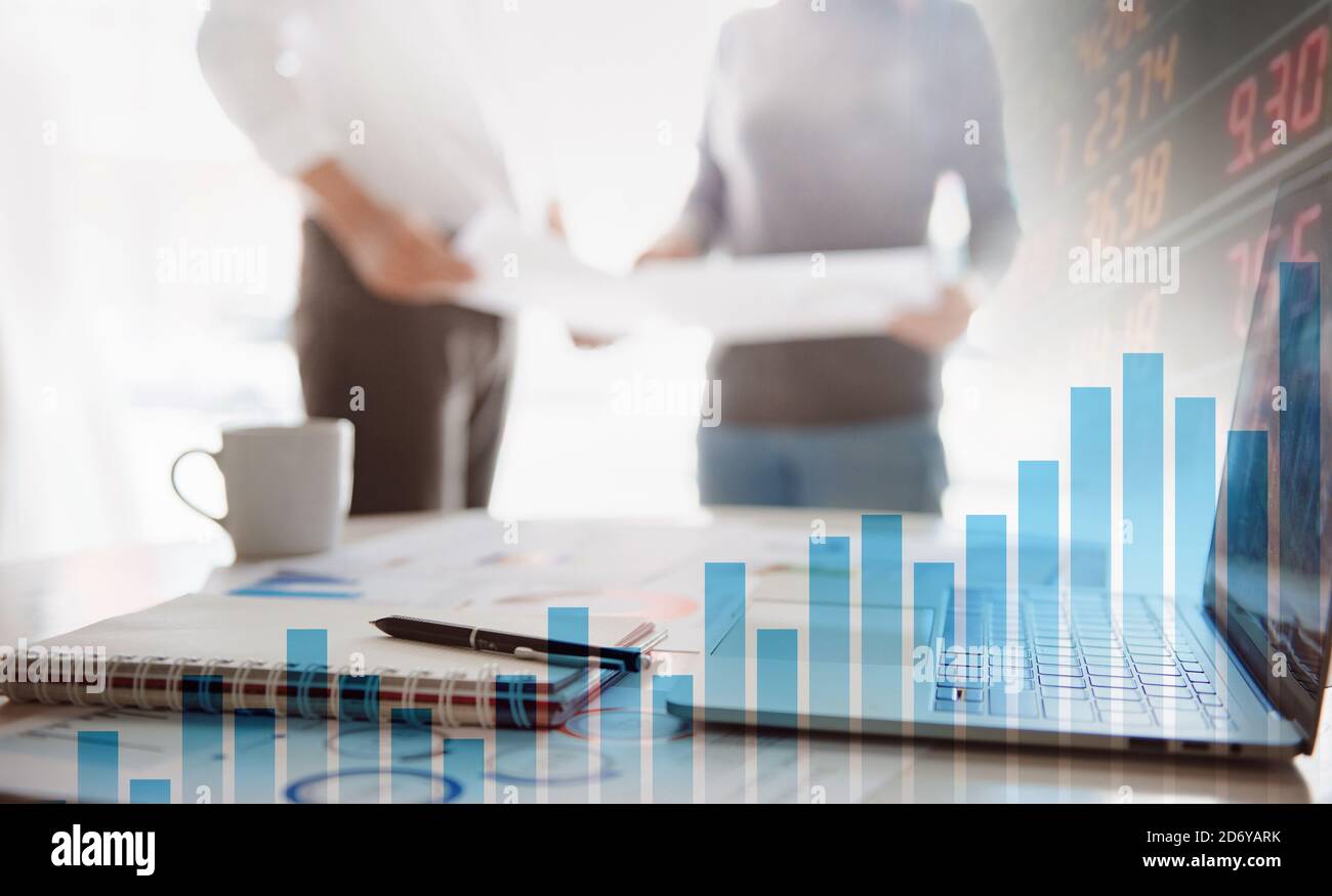 Two business people working together on corporate strategy. Try to analyze statistics. Financial forecast graph hologram. Double exposure. Stock Photo