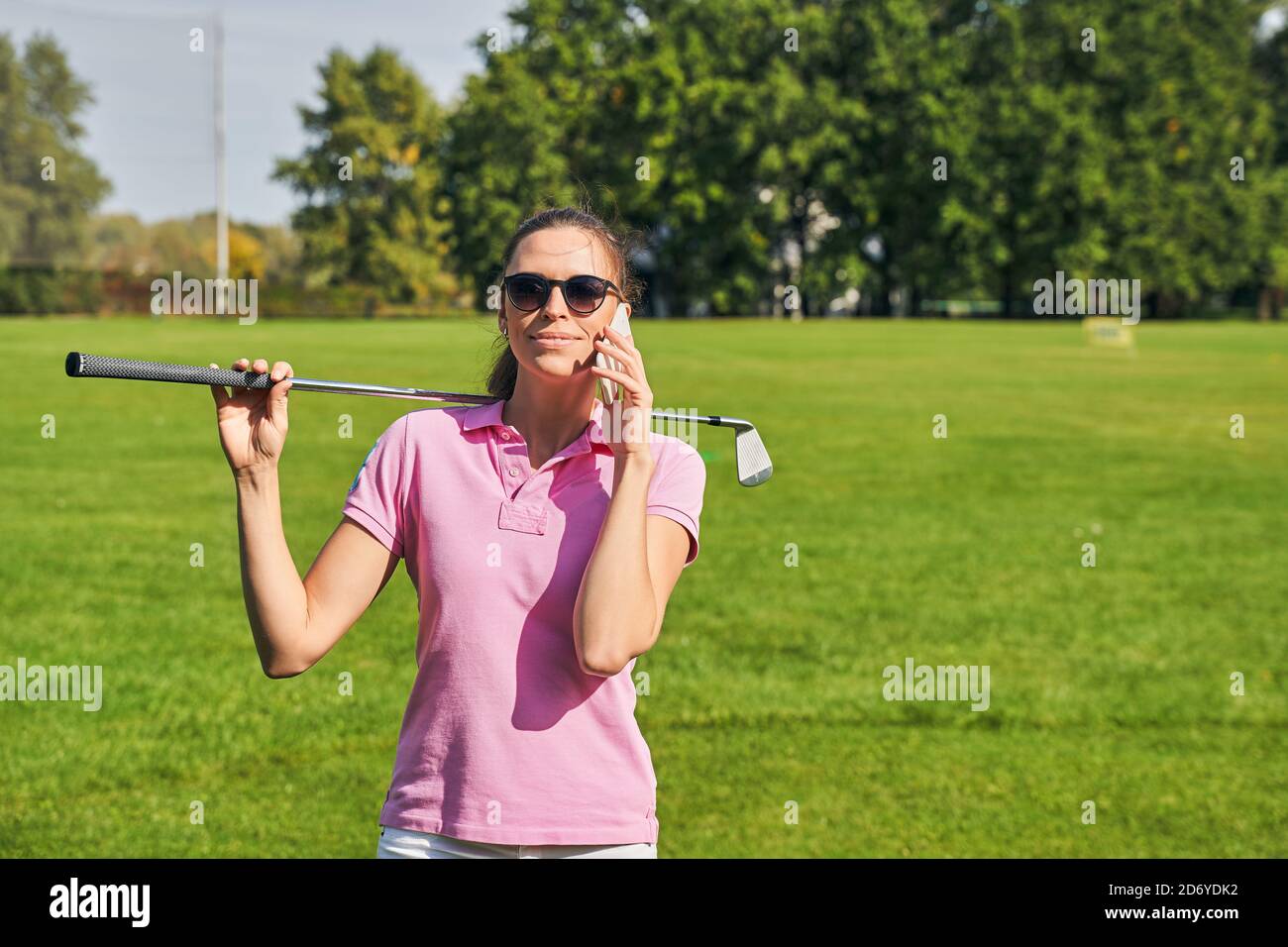 Smiling female with a golf club calling on her cellphone Stock Photo