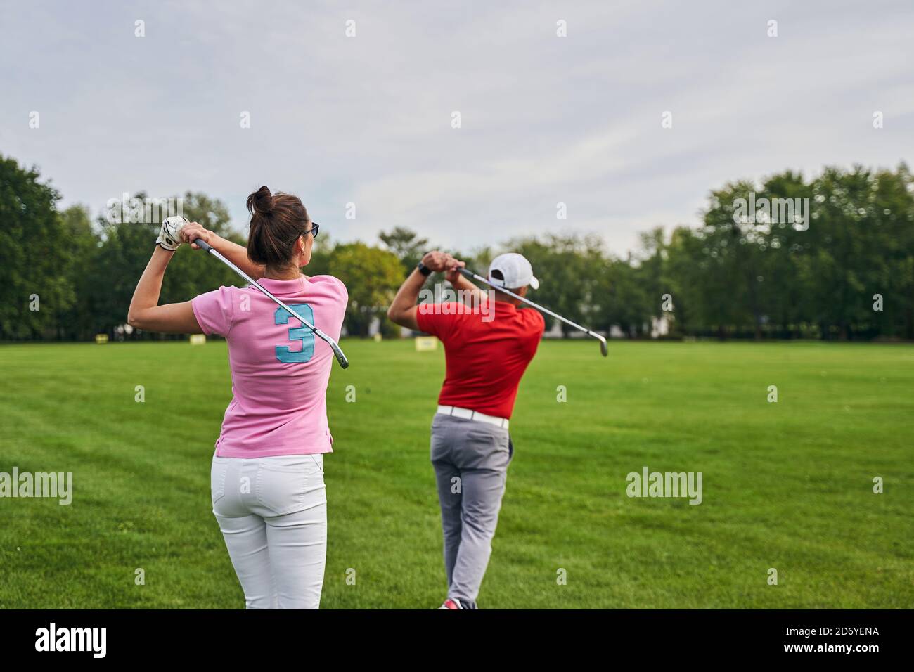 Two athletes practicing golf swings on the driving range Stock Photo