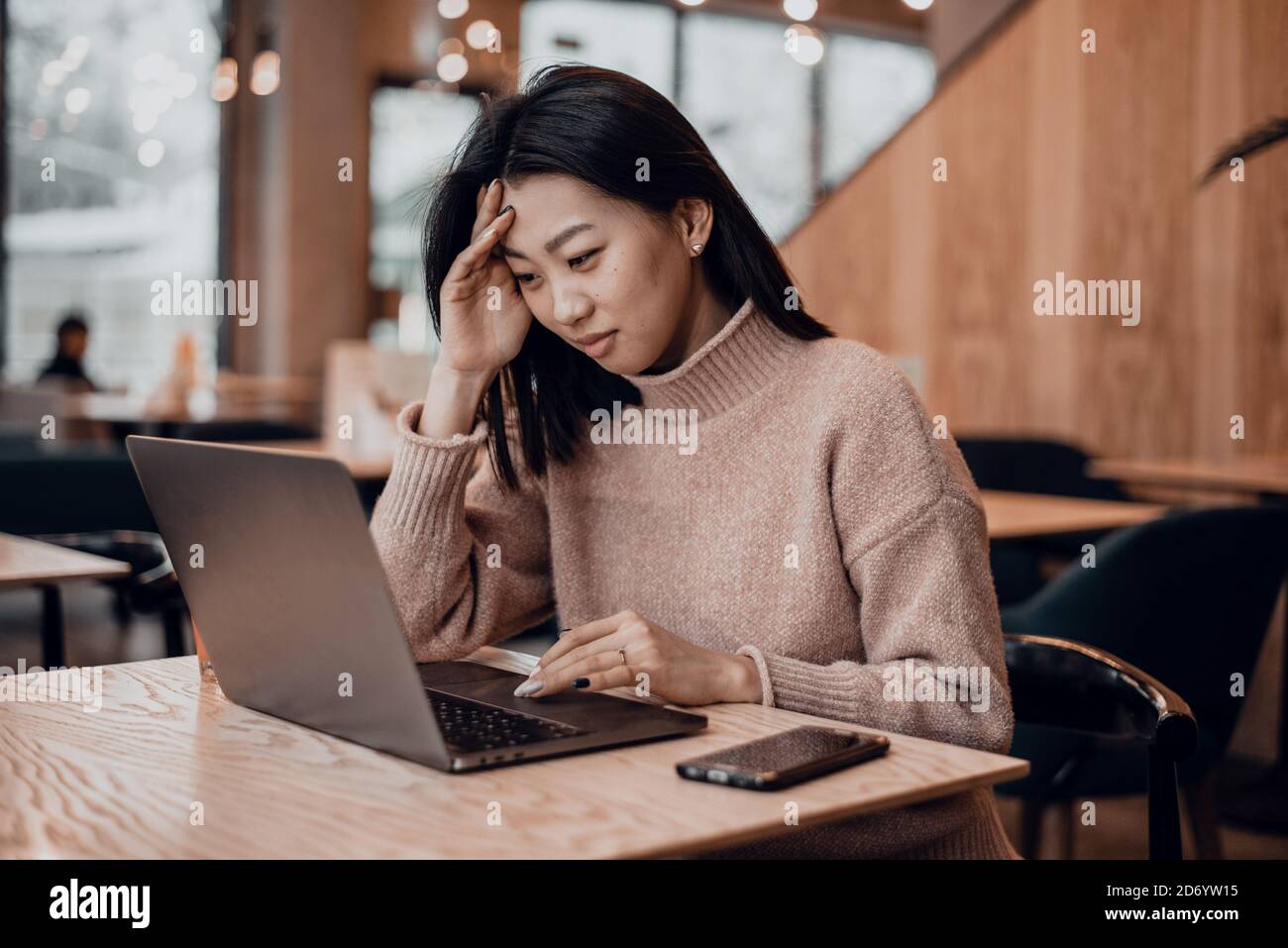The embarrassed girl works in a laptop in a coffee shop and is unhappy with the mistakes. Confused business woman annoyed by online problem, spam email or fake internet news looking at laptop. female worker feeling shocked about stuck computer, bewildered by scam message or virus. Stock Photo