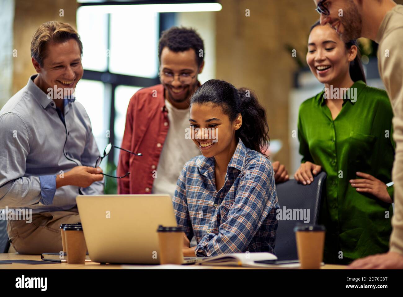 Well done. Group of happy multiracial business people looking at laptop screen, discussing project results and smiling while working together in the modern office or coworking space. Teamwork concept Stock Photo