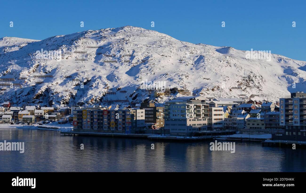 Front view of residential buildings located at the shore in Hammerfest, Norway, Scandinavia at the arctic sea with snow-covered mountains in winter. Stock Photo