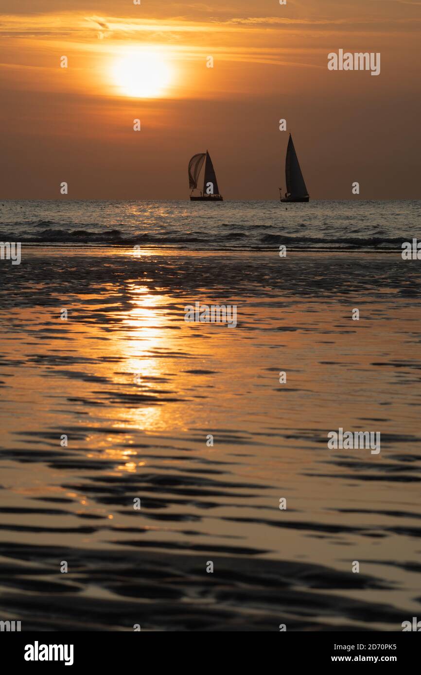 A vertical view of a golden sunset at the sea with two sailing boats in ...
