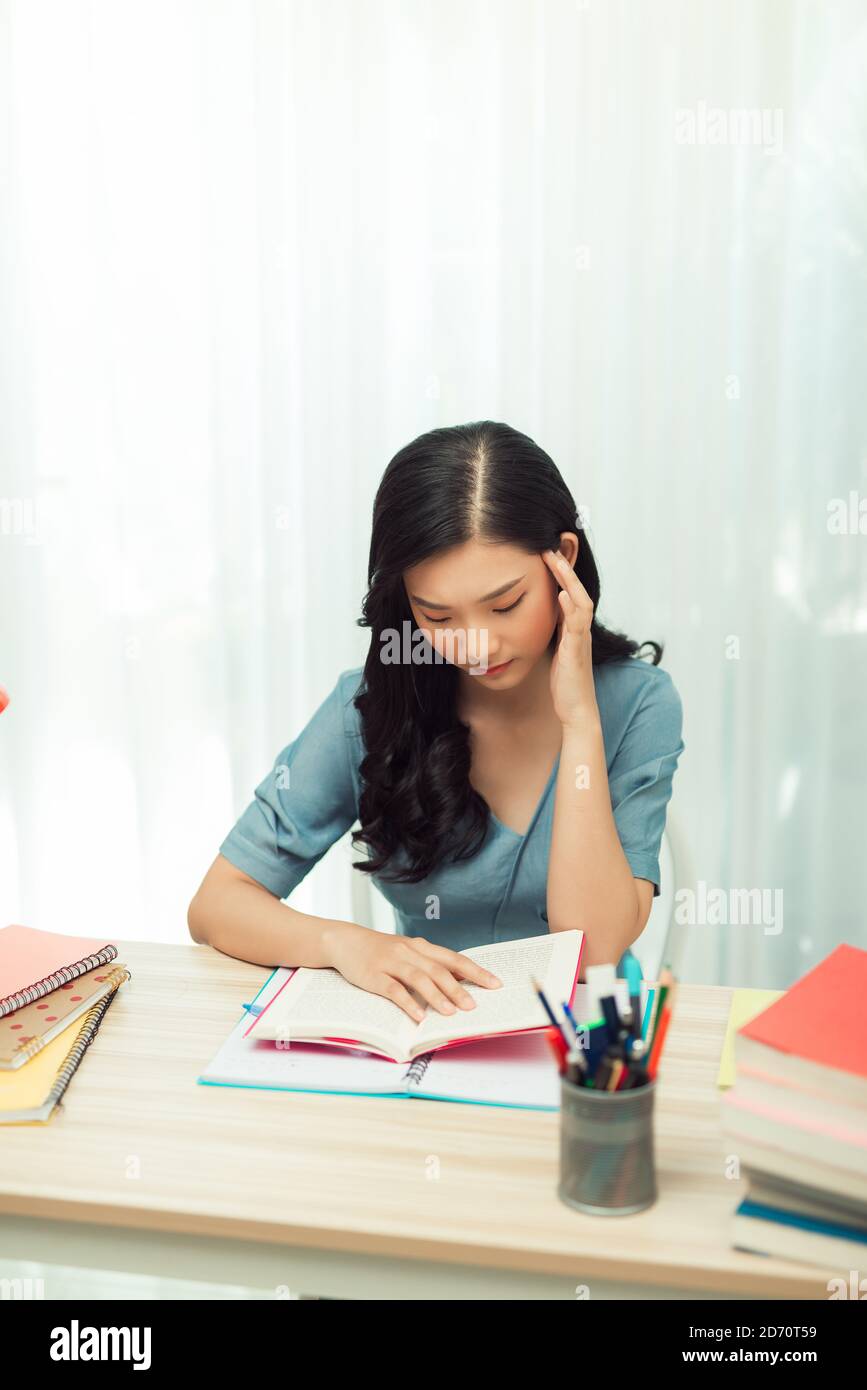 Focused millennial girl studying, preparing for entrance exams or university tests, reading book, taking down notes in textbook. Stock Photo