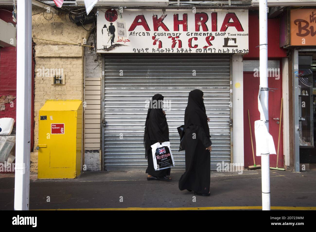 Two muslim women walk past an African clothes store in Shepherd's Bush market in west London. The market sells a multicultural mix of Indian, Polish, African and Caribbean goods. September 30th will mark 100 days since the UK voted to leave the EU, during which time reported anti-immigrant hate crimes have increased. Stock Photo
