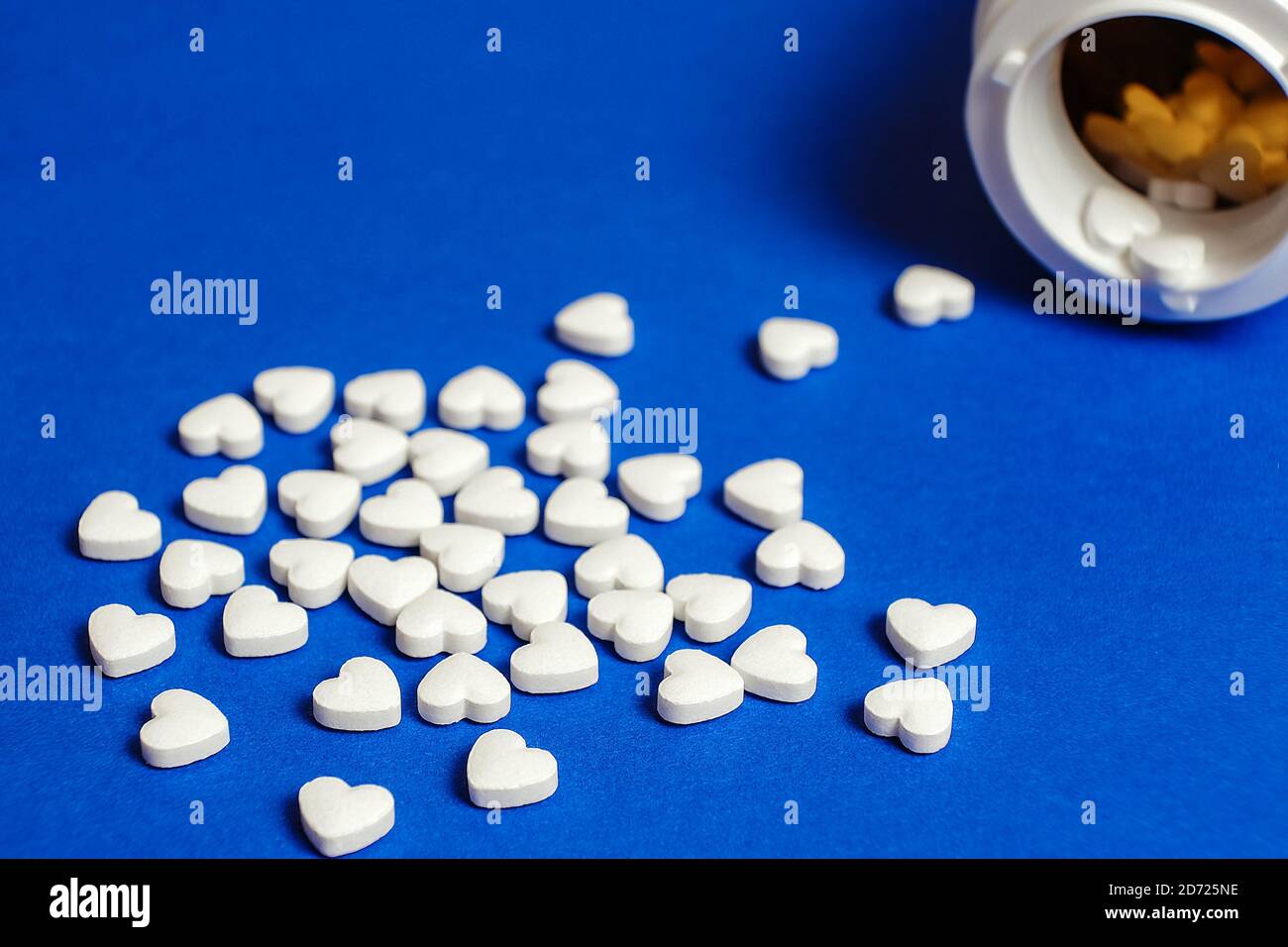 Pills in the shape of a heart poured out from the bottle on the blue surface of the table at the pharmacy. Isolated background. Blue background Stock Photo