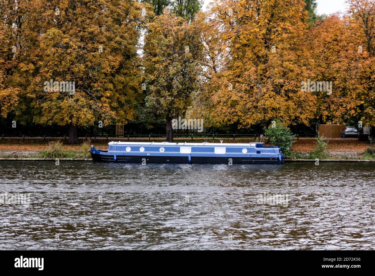 Traditional River Houseboat Moored On The River Bank With Golden Autumn Trees In The Background Stock Photo