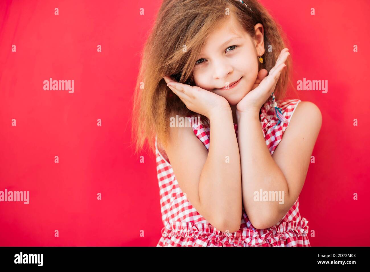Little, blonde girl looking cute, hands under chin. Copy space, isolated on pink background Stock Photo